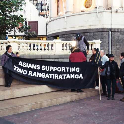 A group of people holding a large black banner saying 'Asians Supporting Tino Rangatiratanga'