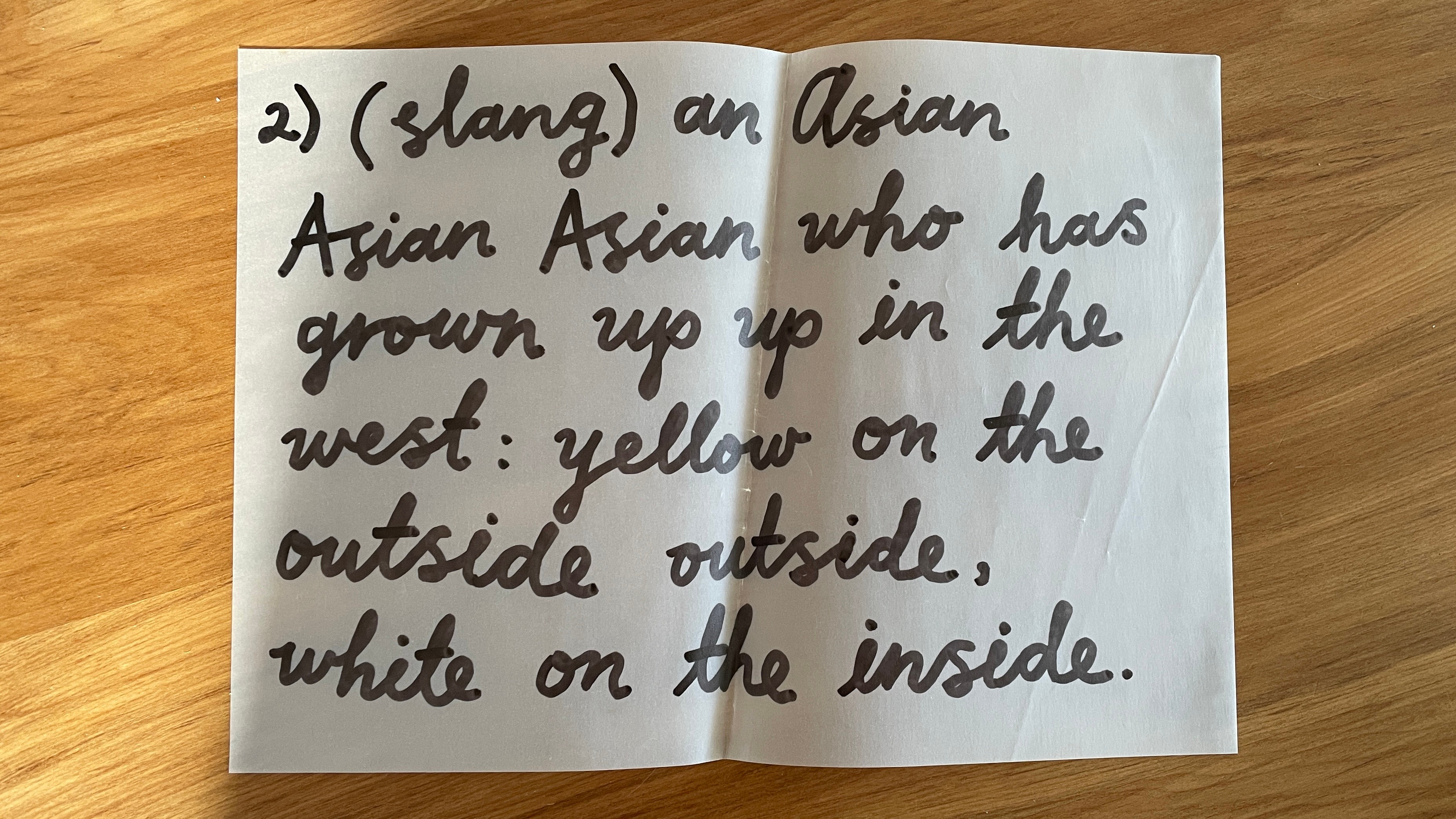 A piece of paper with the following handwriting: “2) (slang) an Asian Asian Asian who has grown up up in the west: yellow on the outside outside, white on the inside.”