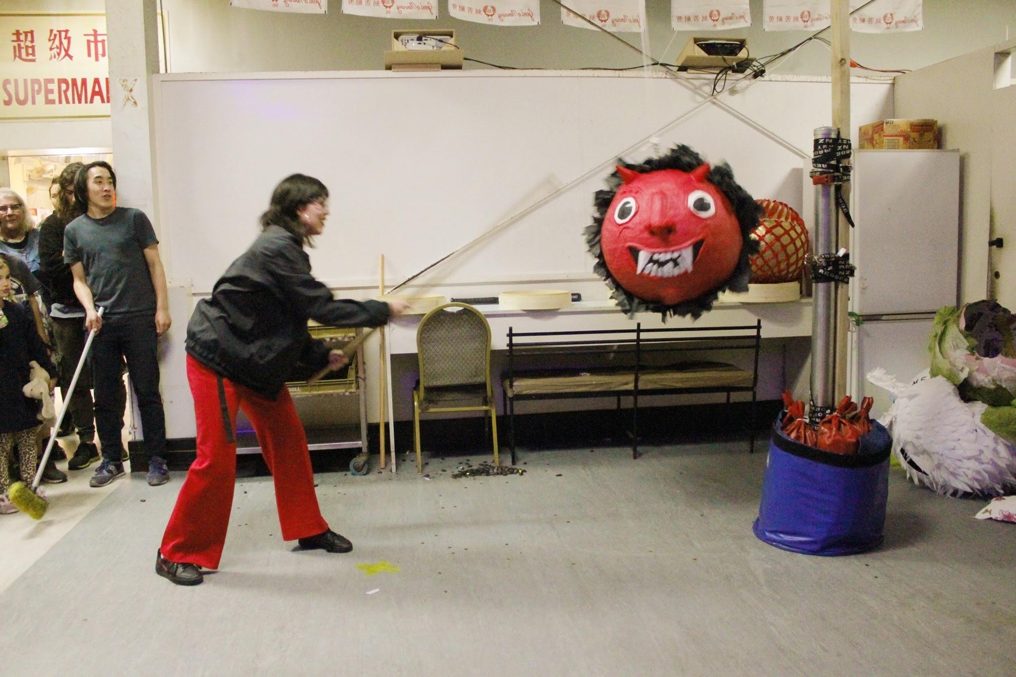 A woman in red smashing a demon piñata with a stick