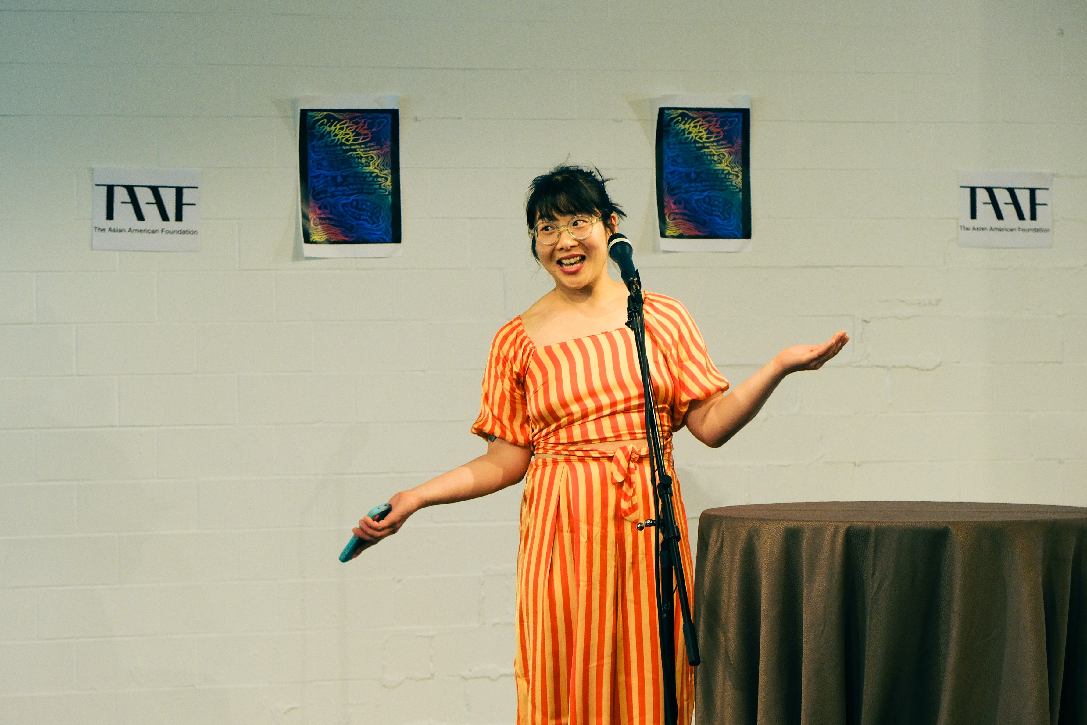 Rose Lu in an orange striped dress stands on stage with a microphone.