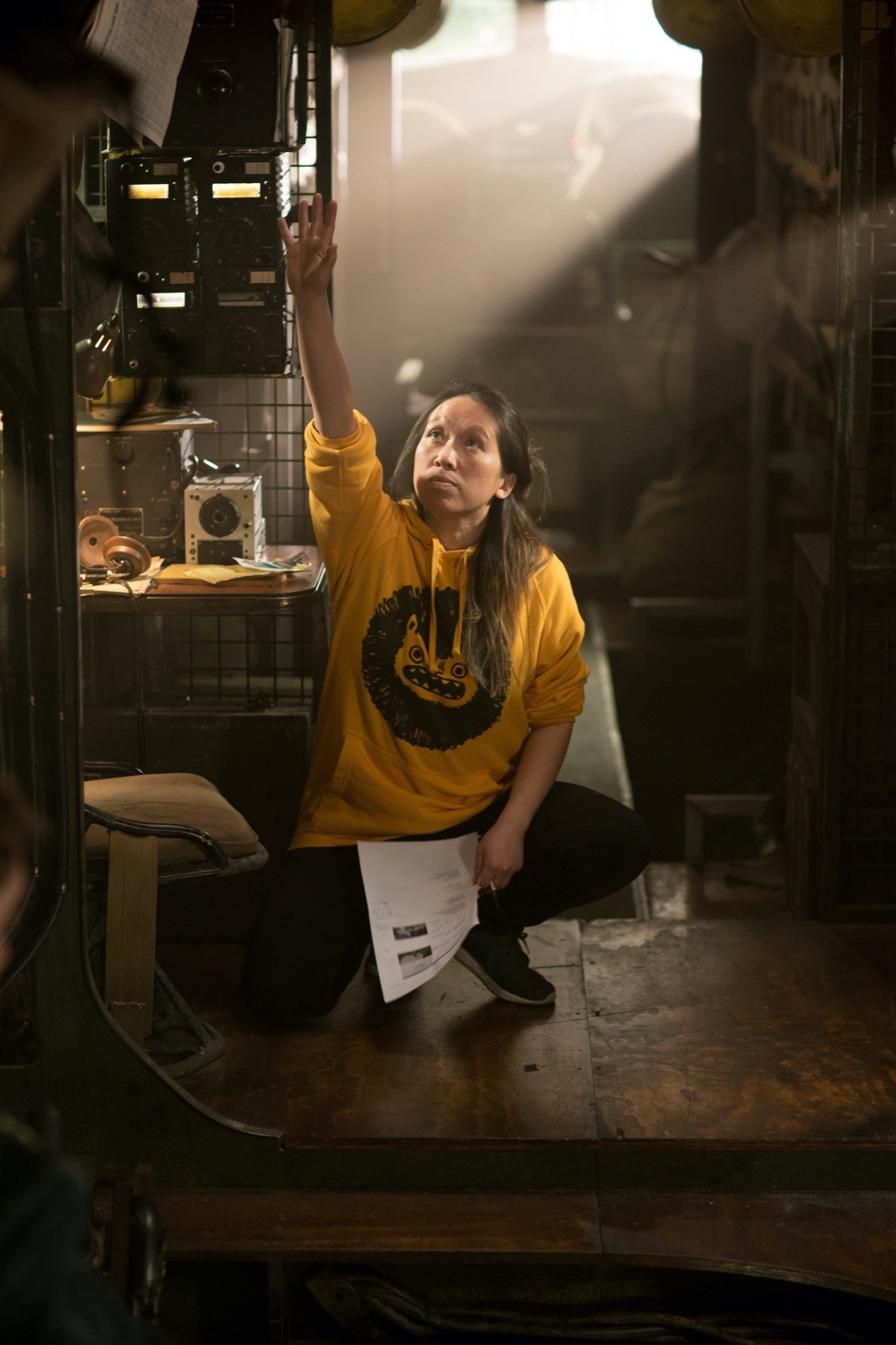 A Chinese woman squatting pointing in the air holding a piece of paper