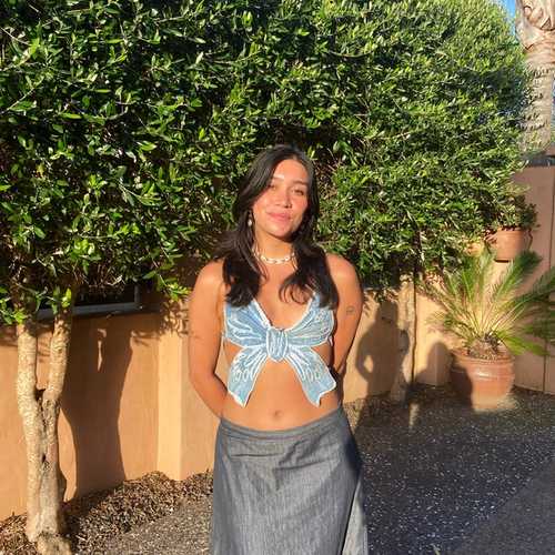 Person in a blue ribbon top and long grey skirt wearing a shell necklace being photographed during the golden hour