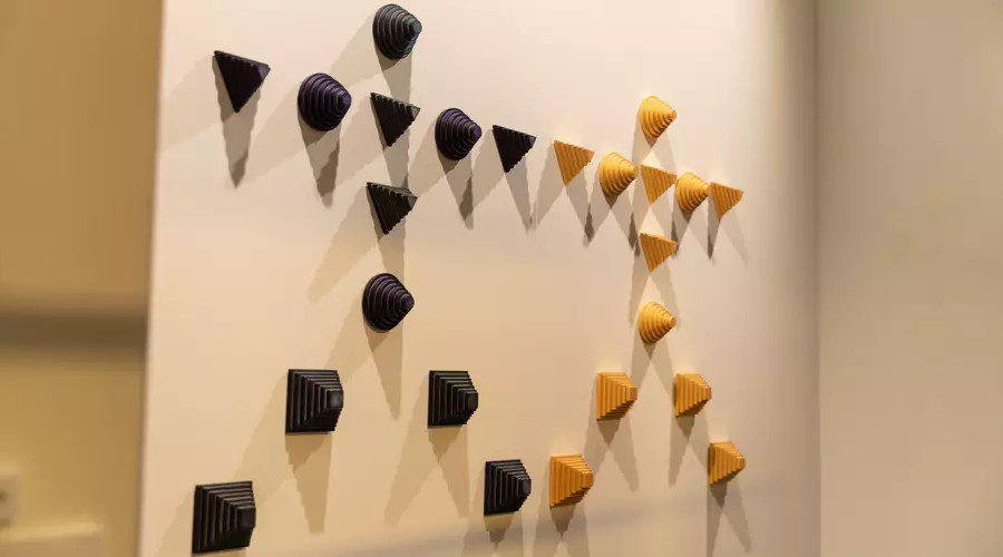 Purple and yellow cone-shaped objects arranged on a white wall in human-figure shapes.