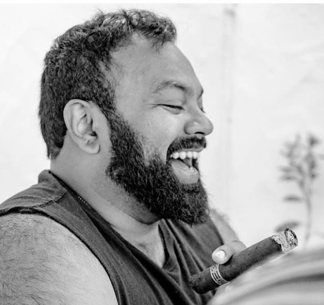 A black and white photo of a man laughing and holding a cigar