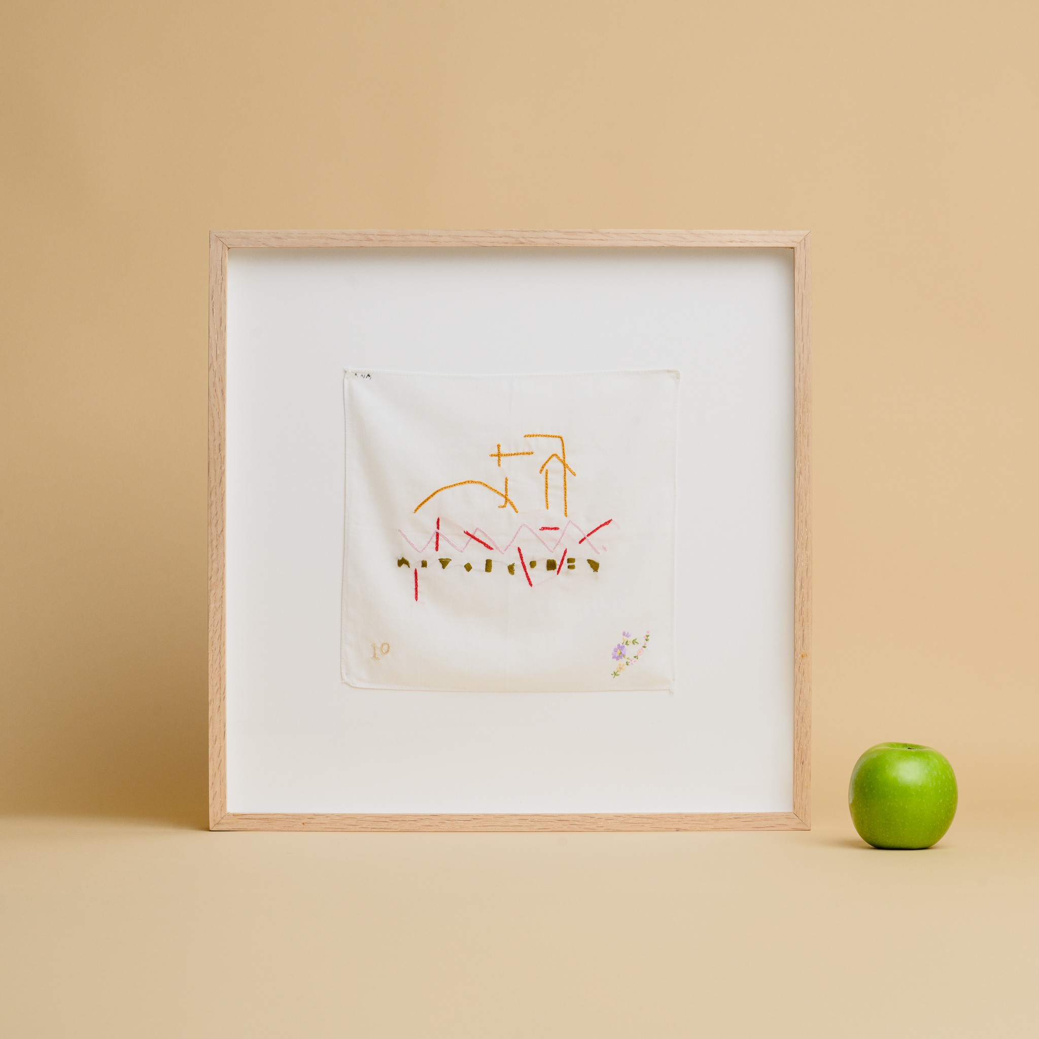 An embroidered handkerchief framed in a light pine frame 