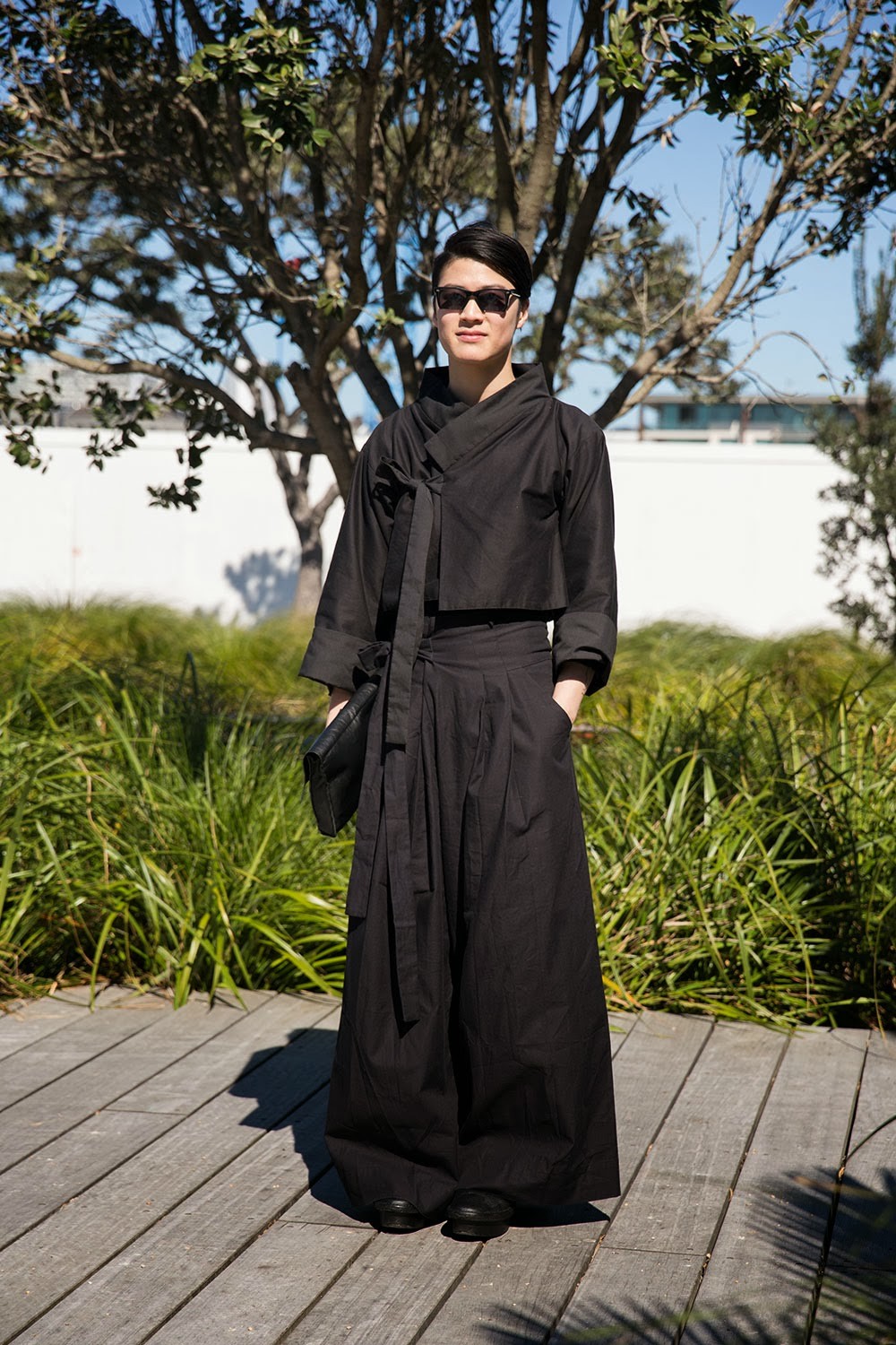 Steven standing on a boardwalk wearing a black handmade outfit with Korean influences.