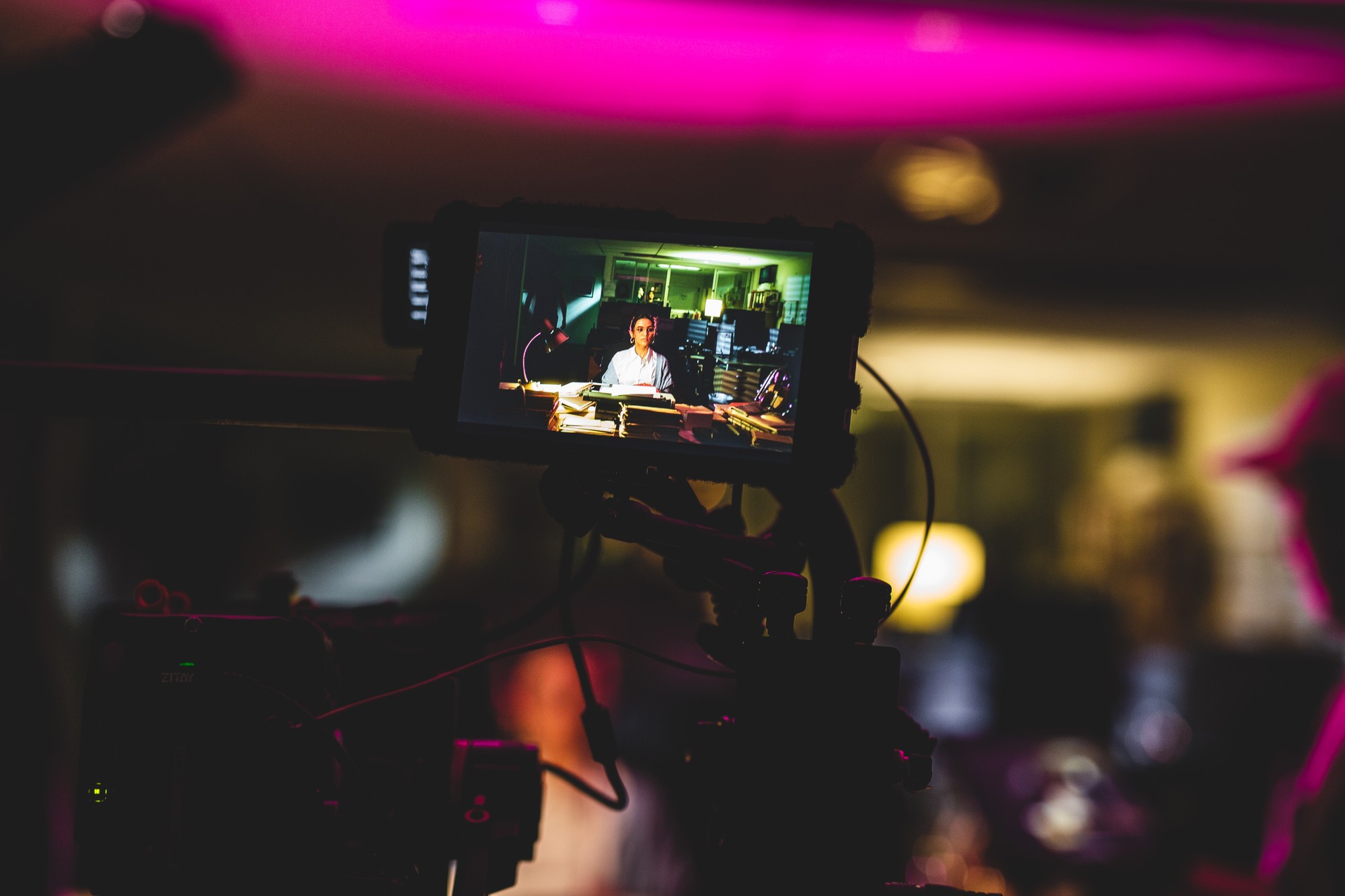 Monitor on a camera, fillming a woman sitting at a desk. 