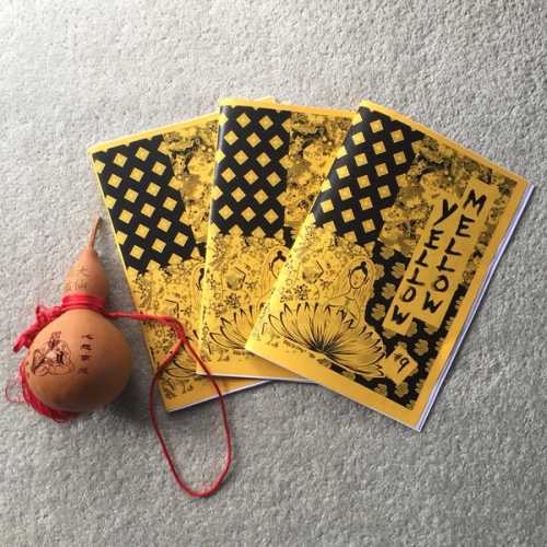Three zines with black and yellow collaged covers displayed next to traditional Chinese object.