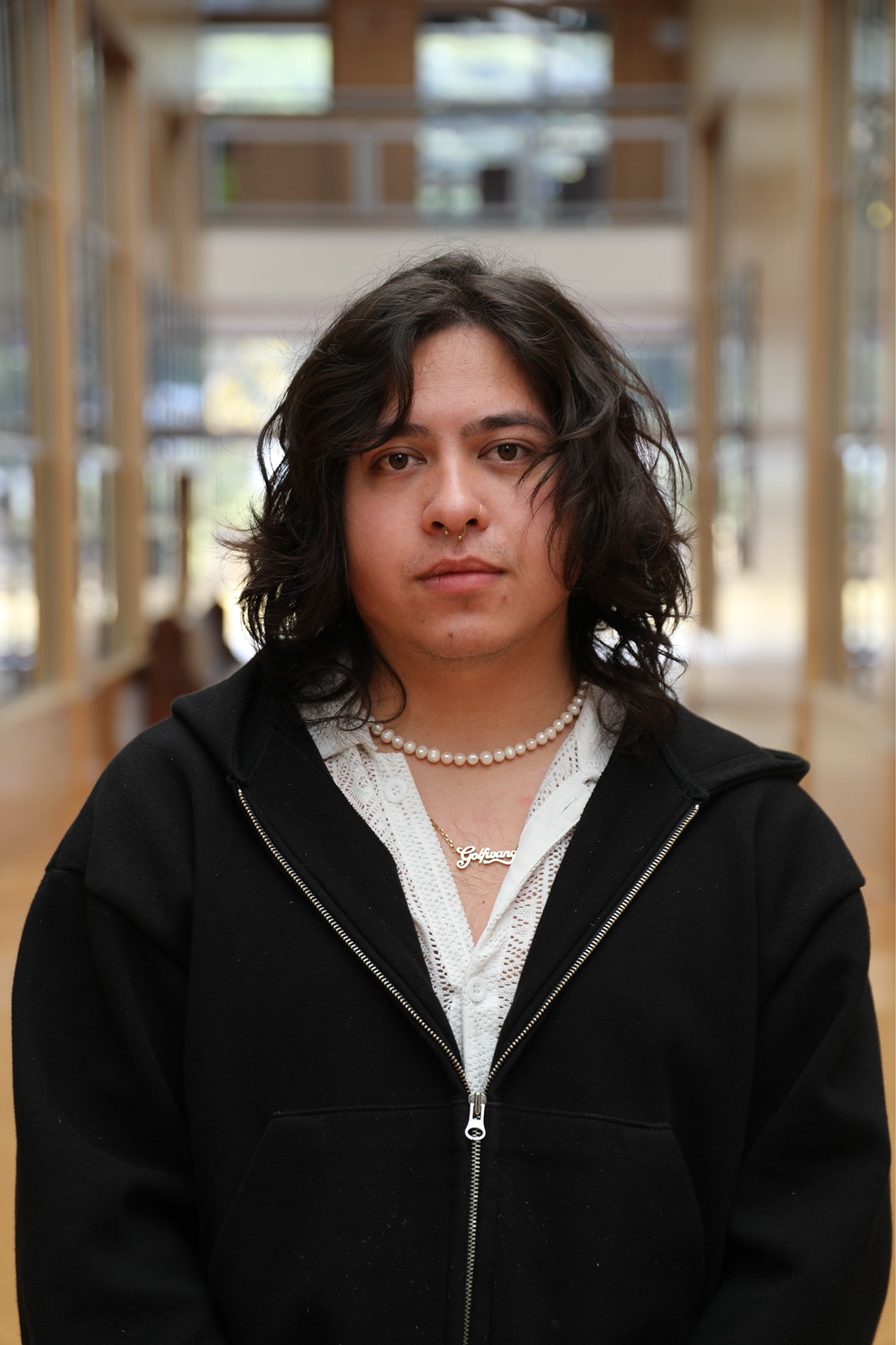 Person with stylish unkempt hair looking into the camera wearing a pearl necklace and fashionable clothes