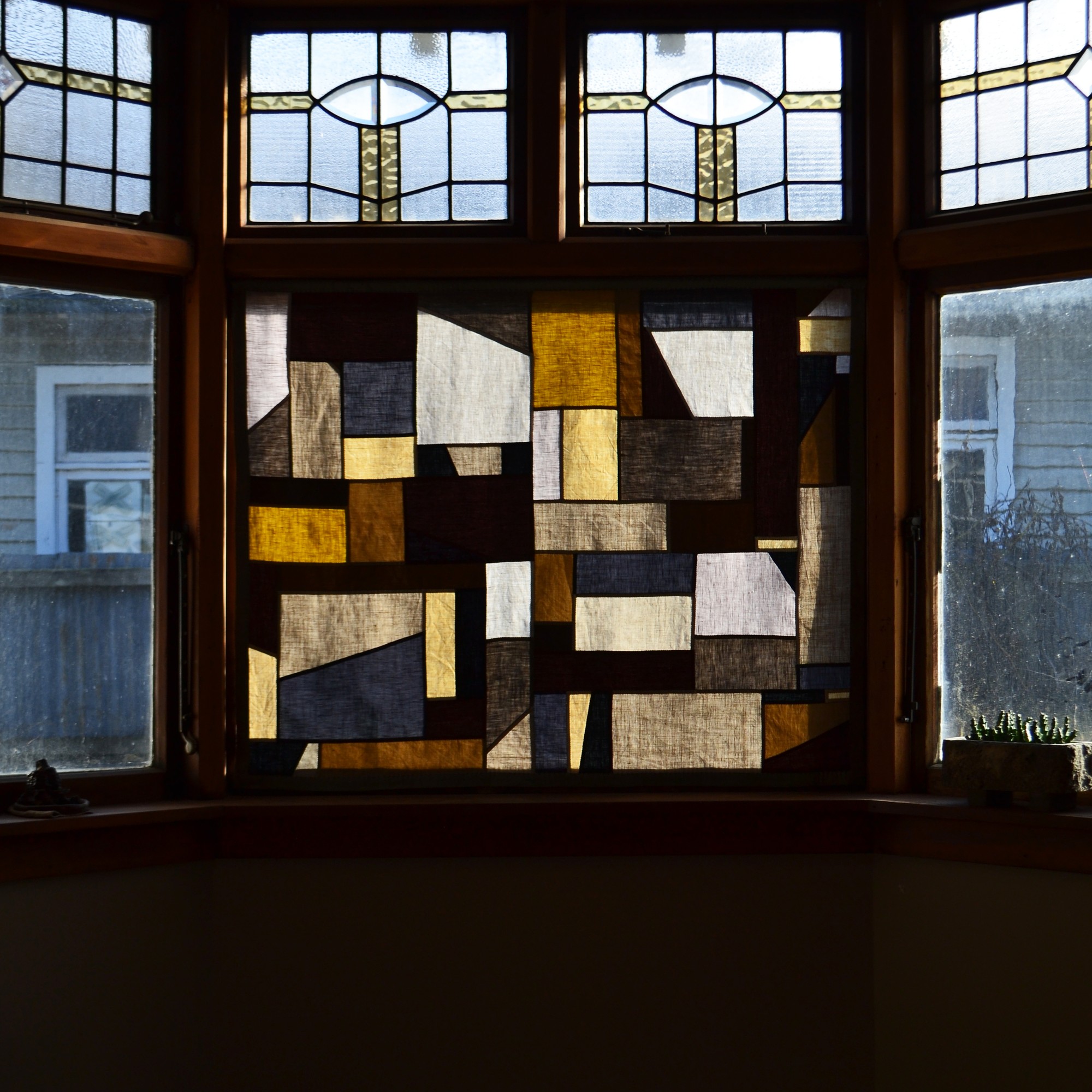 A patchwork fabric hanging in a window with the light shining through.