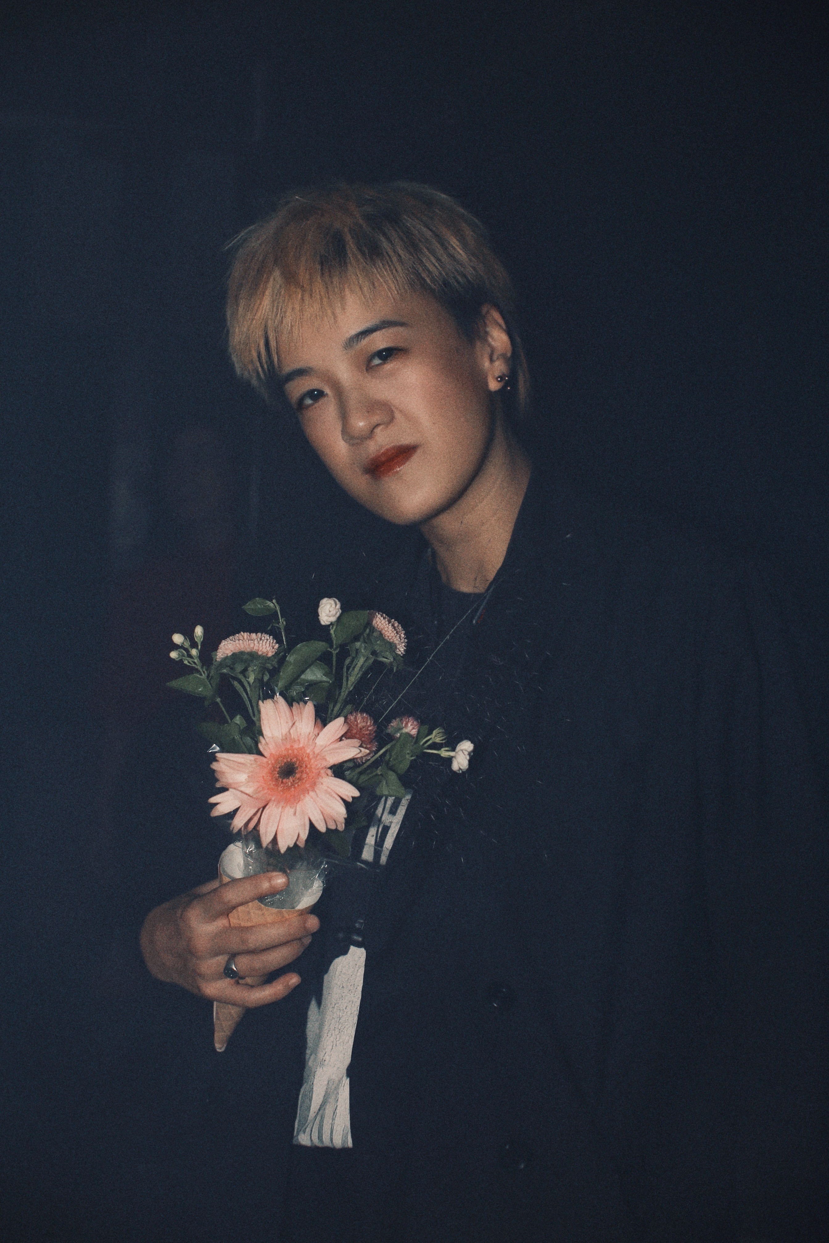 Kristen Ng holding a bouquet of flowers, illuminated by the camera flash