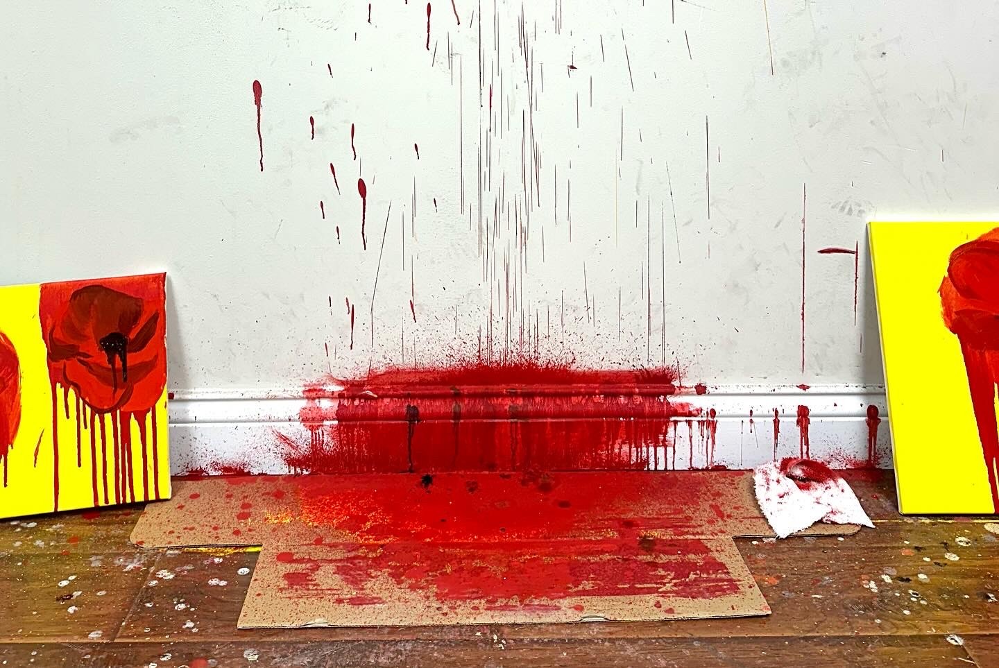 Red paint drips down a wall and pools on a skirting board and piece of cardboard on the floor.