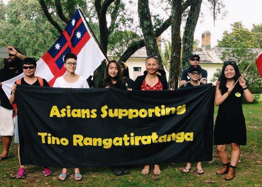 A group of six people holding a black banner with yellow text saying 'Asians Supporting Tino Rangatiratanga'
