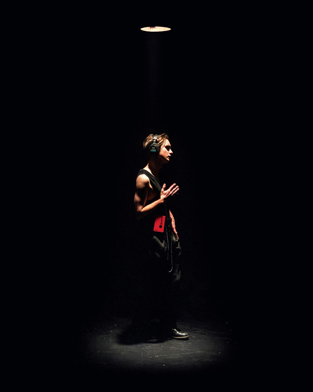 Person wearing headphones and wearing a singlet is being dramatically lit from a lamp above their head