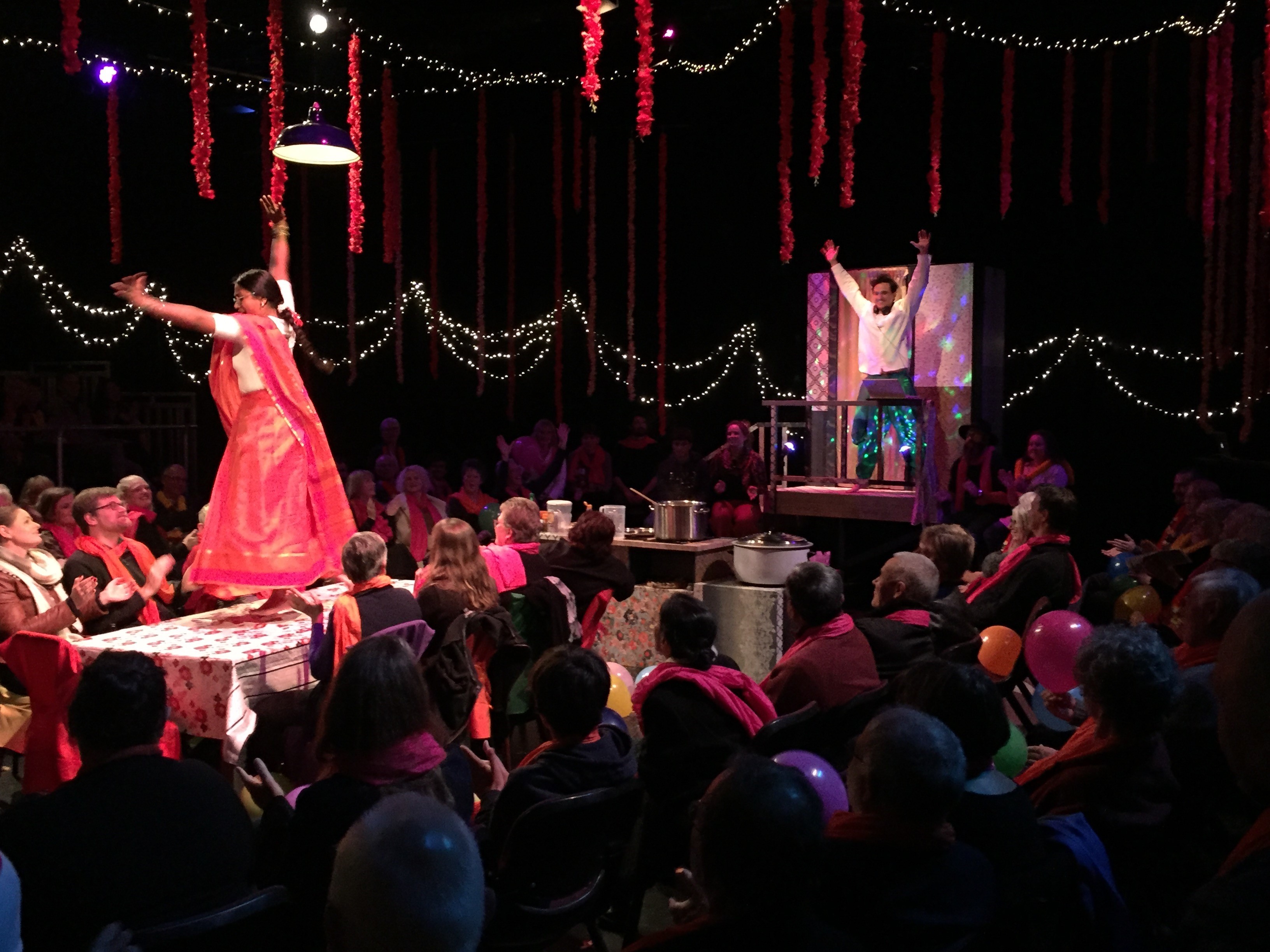 Two people standing on the tables dancing, surrounded by audience gazing upwards