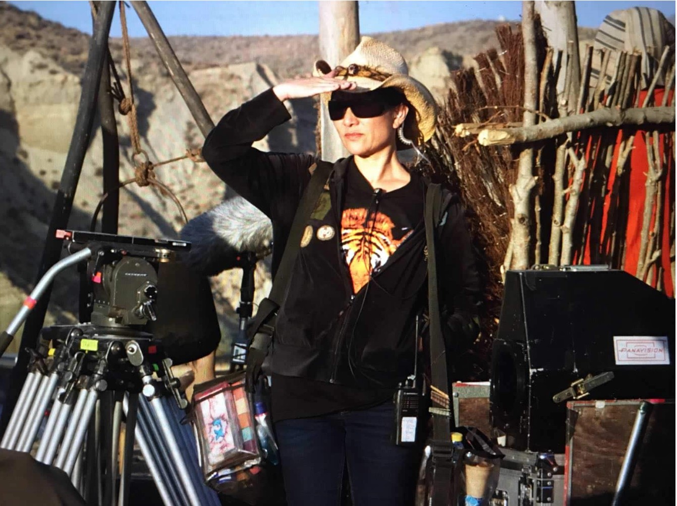 Woman wearing sunglasses and a hat with her hand shielding her eyes from the sun surrounded by film gear.