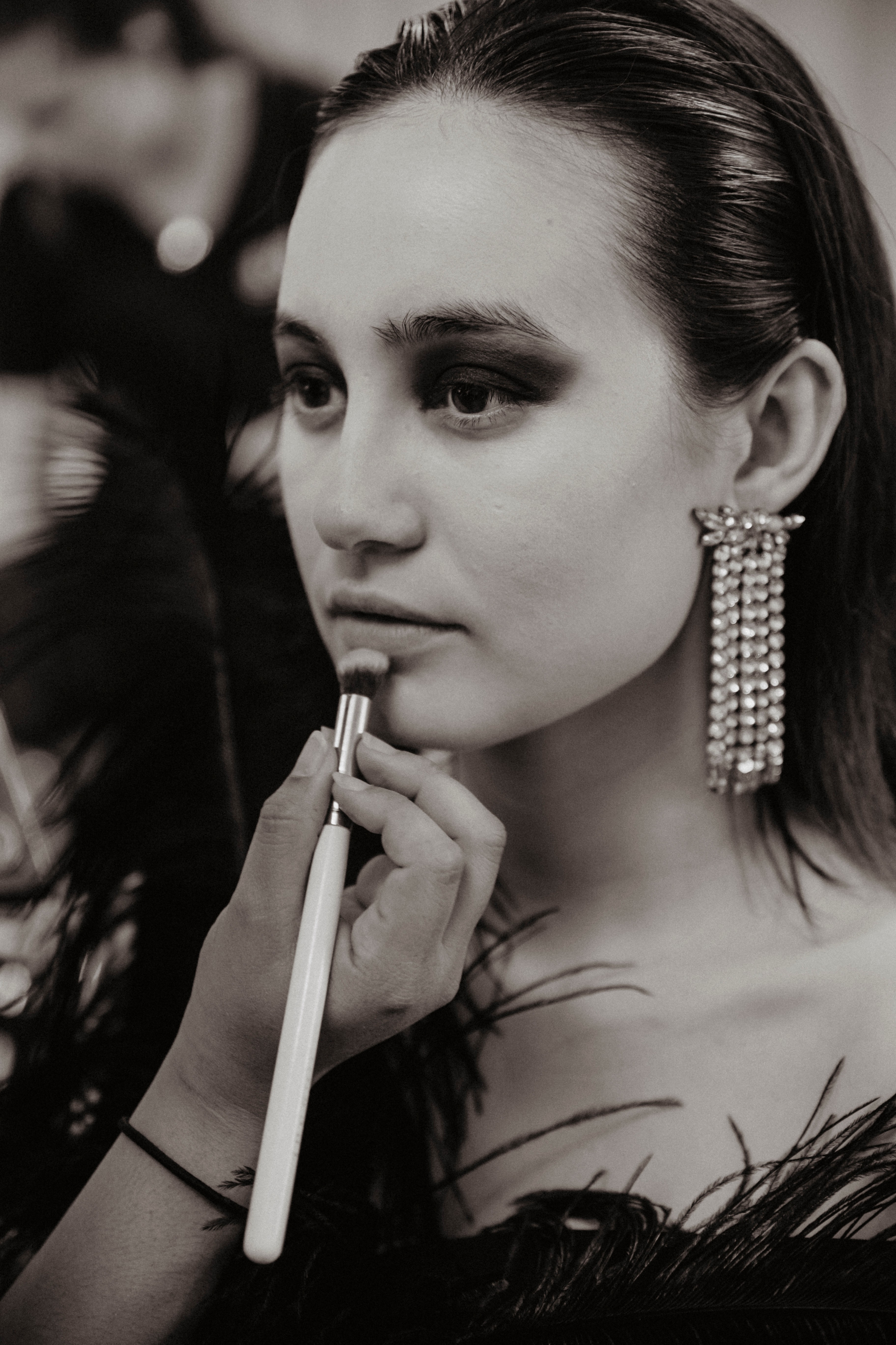 Black and white photo of woman having lipstick brushed onto her with long diamond earrings