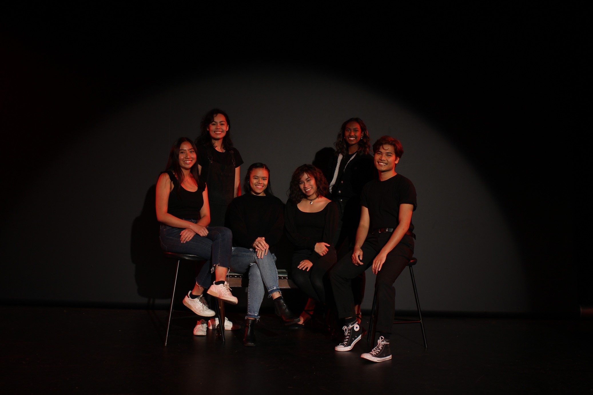 Various smiling Asian people wearing black shirts posing in front of a black background