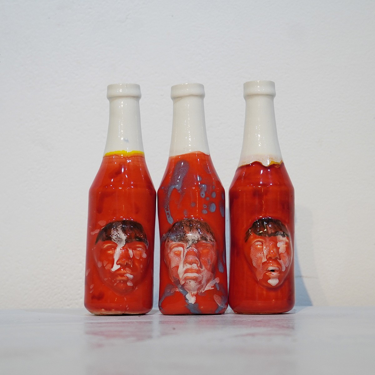 Three chilli sauce bottles with faces painted on them.