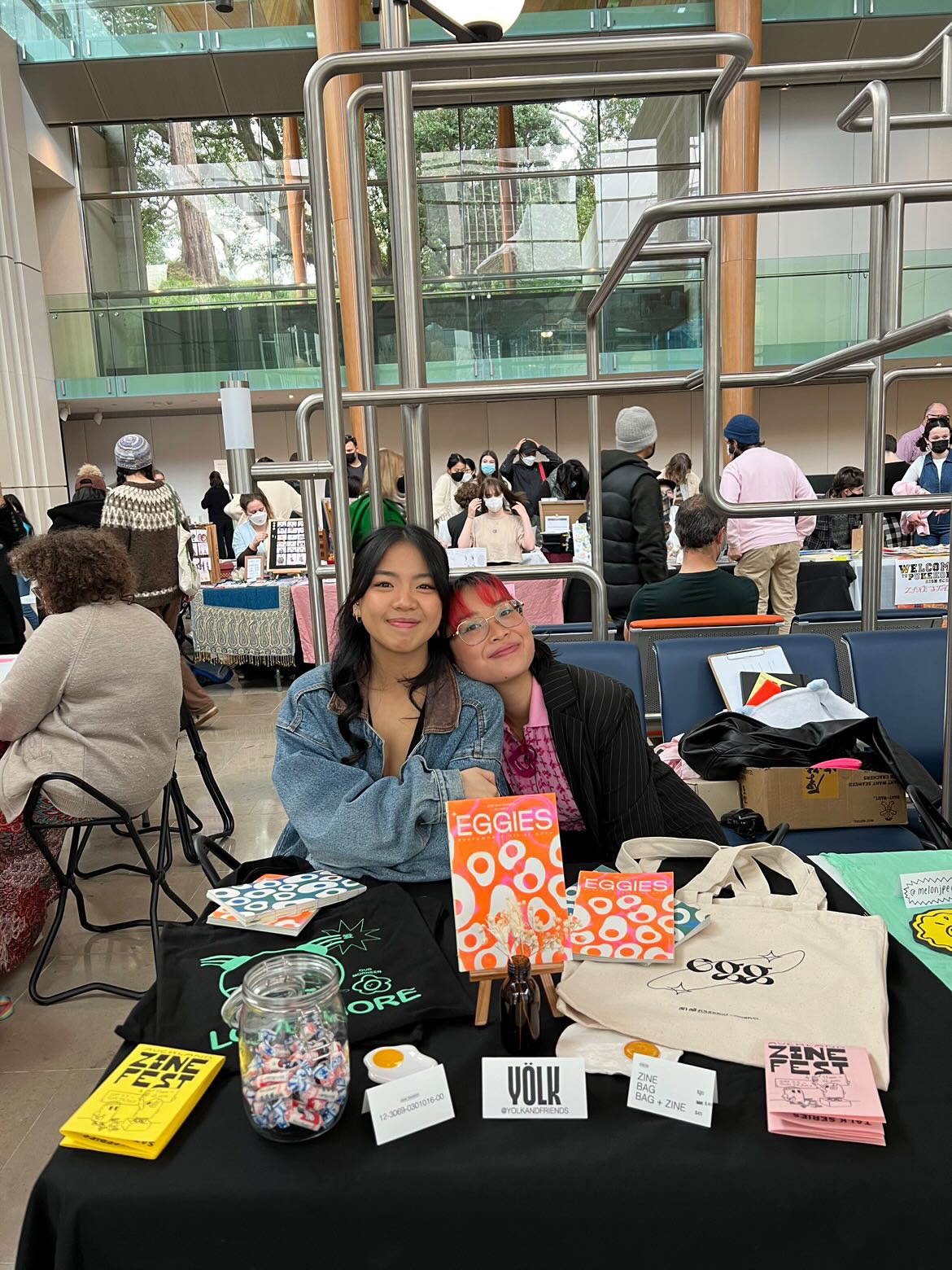 Two people smiling in front of a zine table.