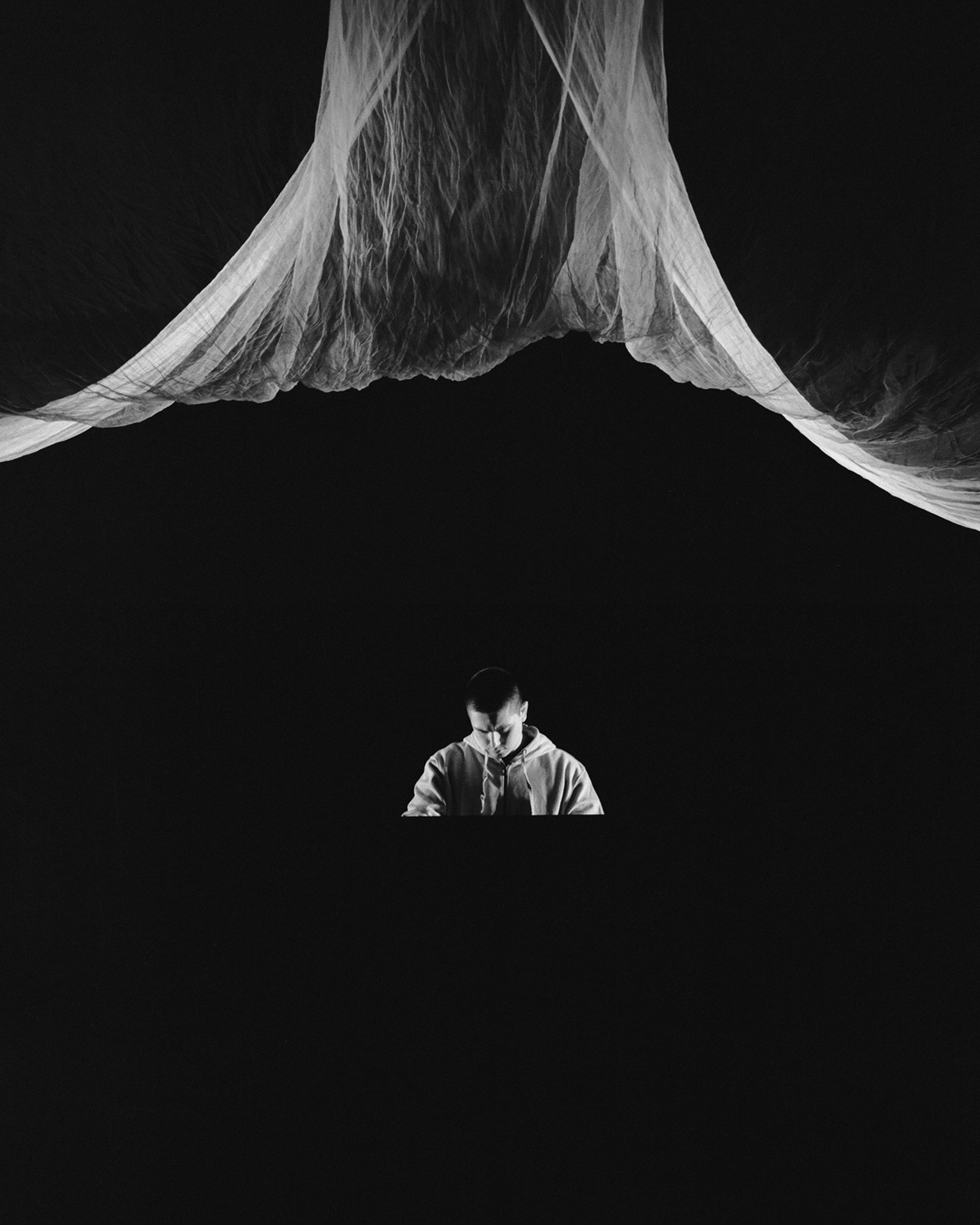 Dramatic black and white photo of a man looking down with a fabric floating above him