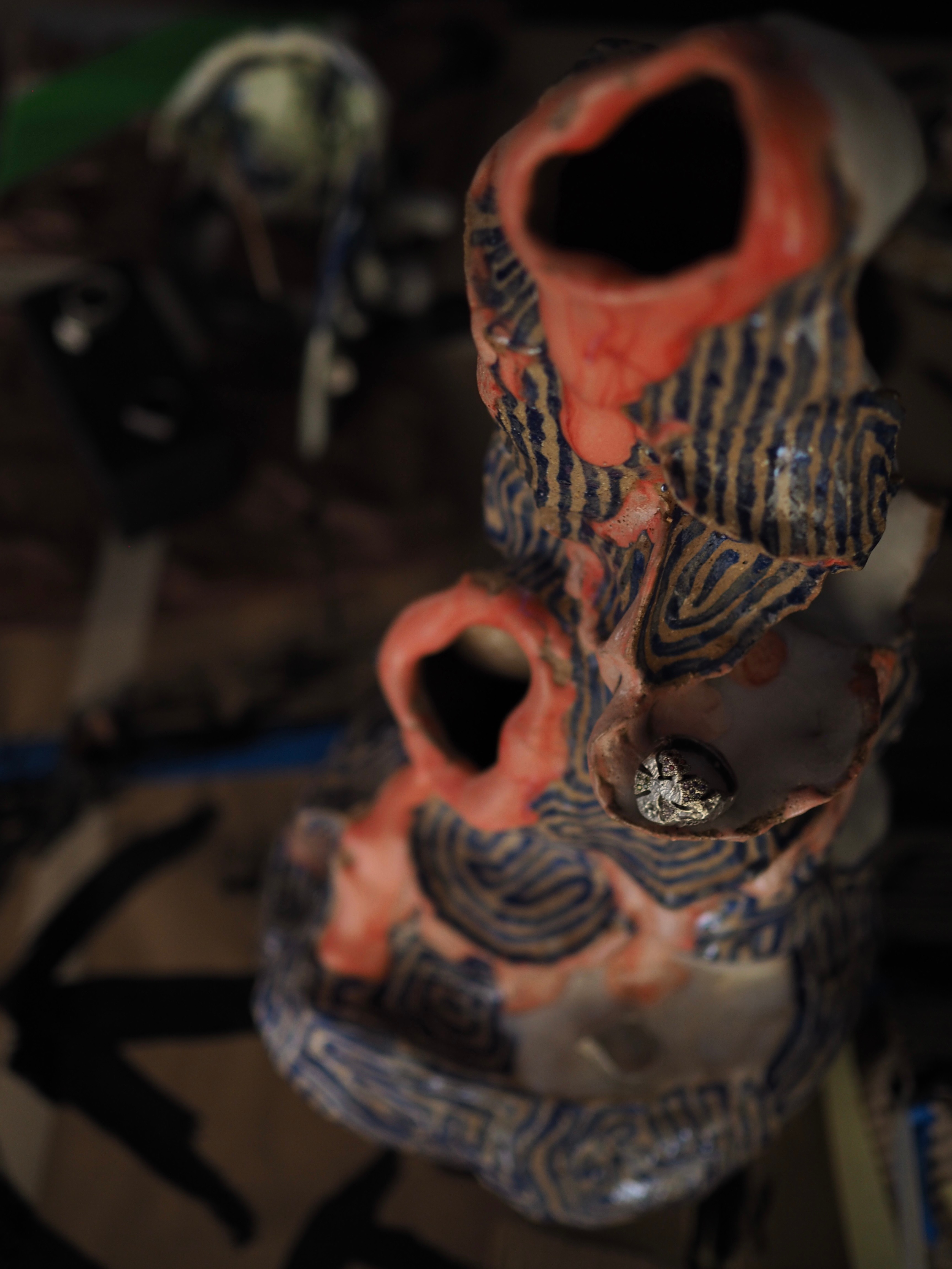 An organic sculpture with multiple holes outlined in orange and blue lines on the body