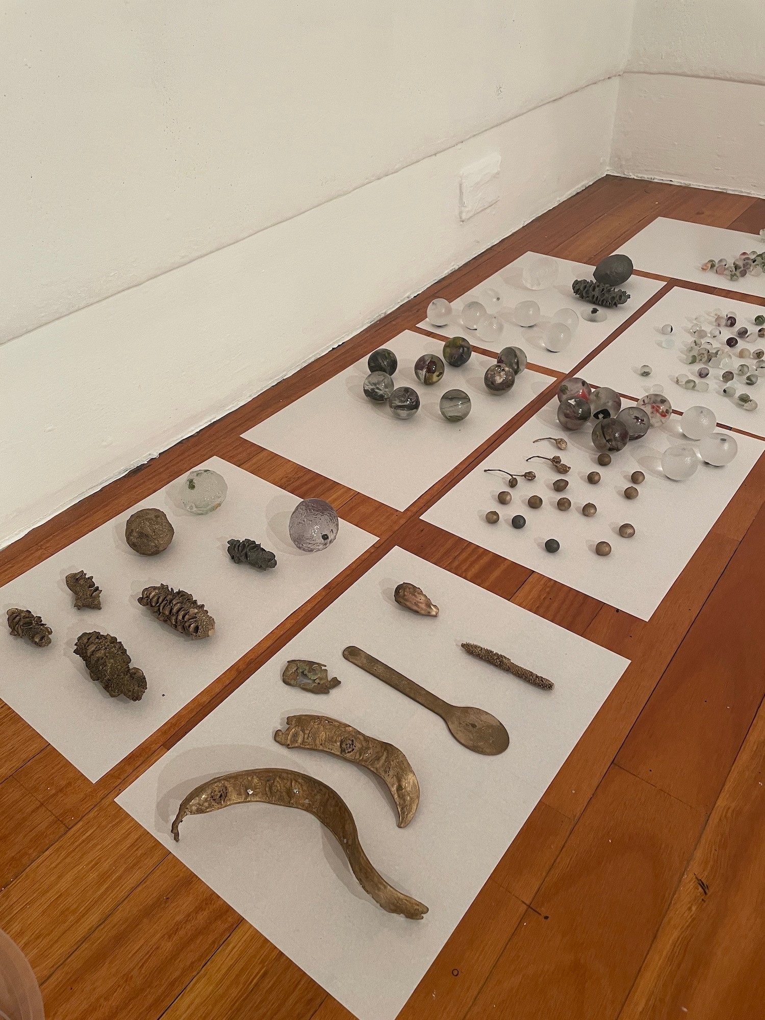 Cast objects laid out on pieces of paper on a wooden floor in the corner of a room