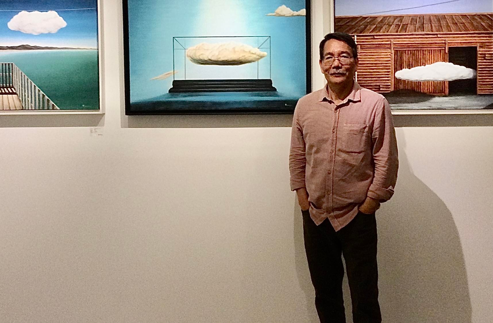 Photo of a man standing in front of a wall of paintings