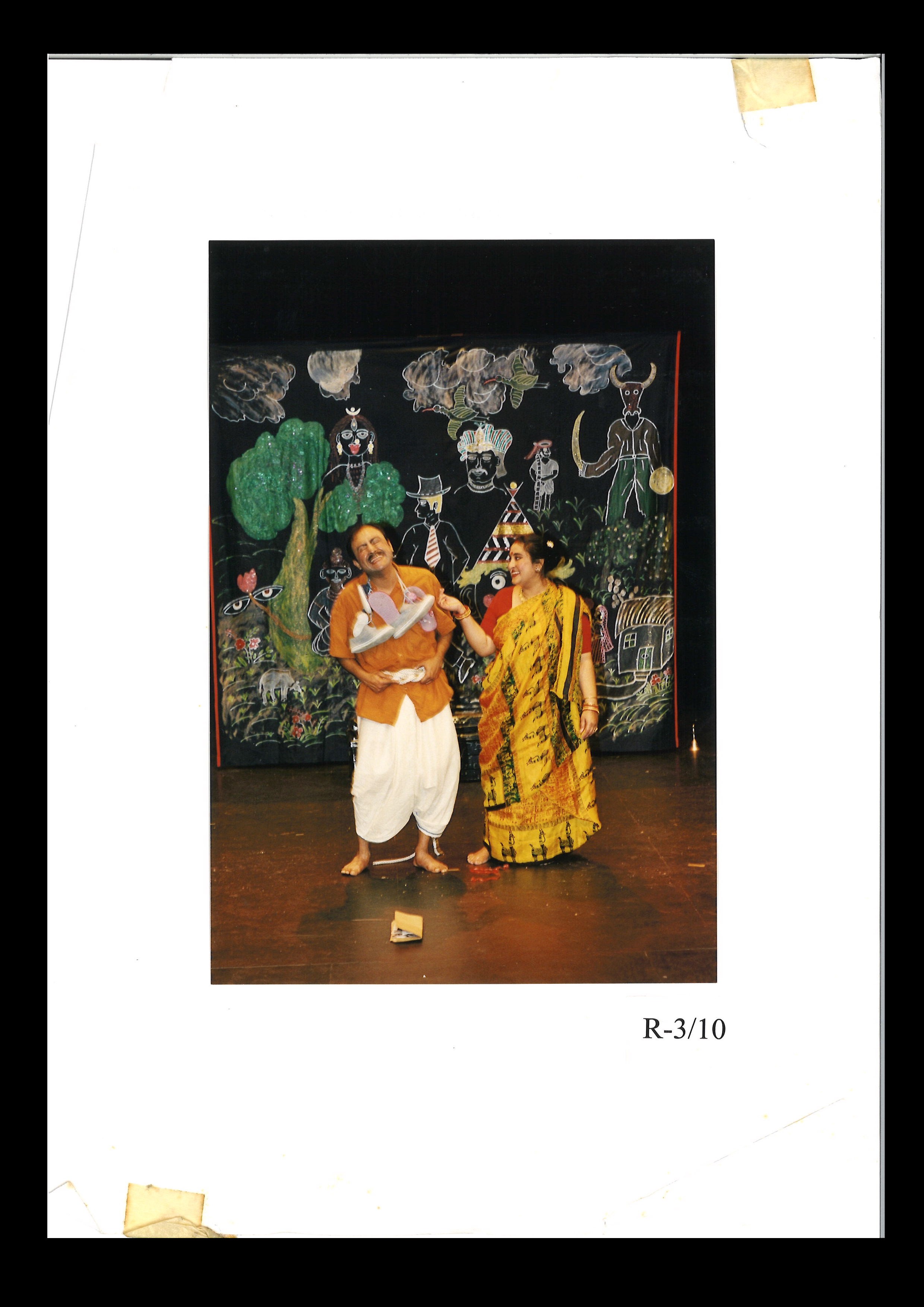 Photo of two actors on stage in front of a colourful backdrop.