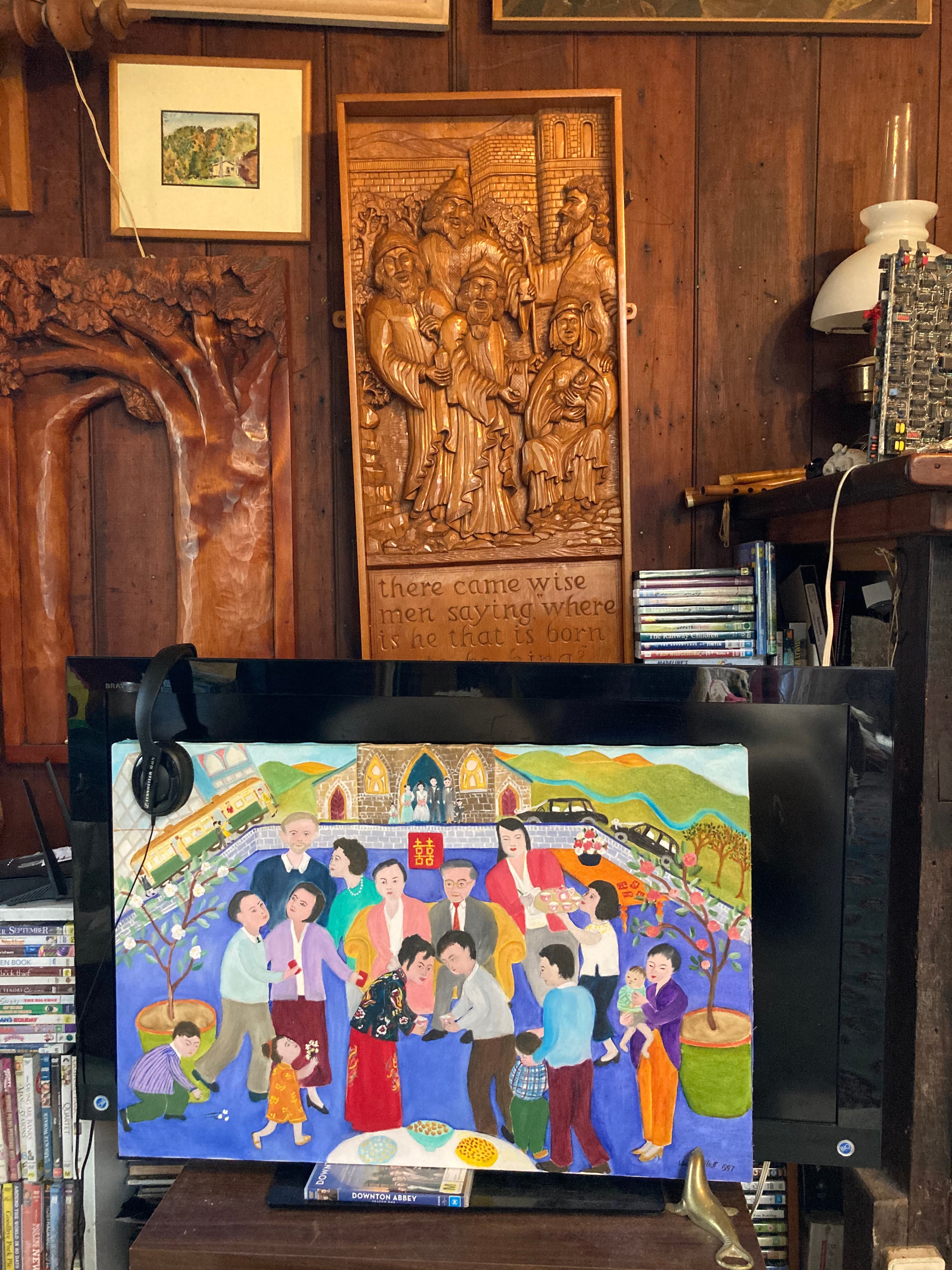 A painting of a family scene at Chinese new Year, beneath a carved wooden panel.