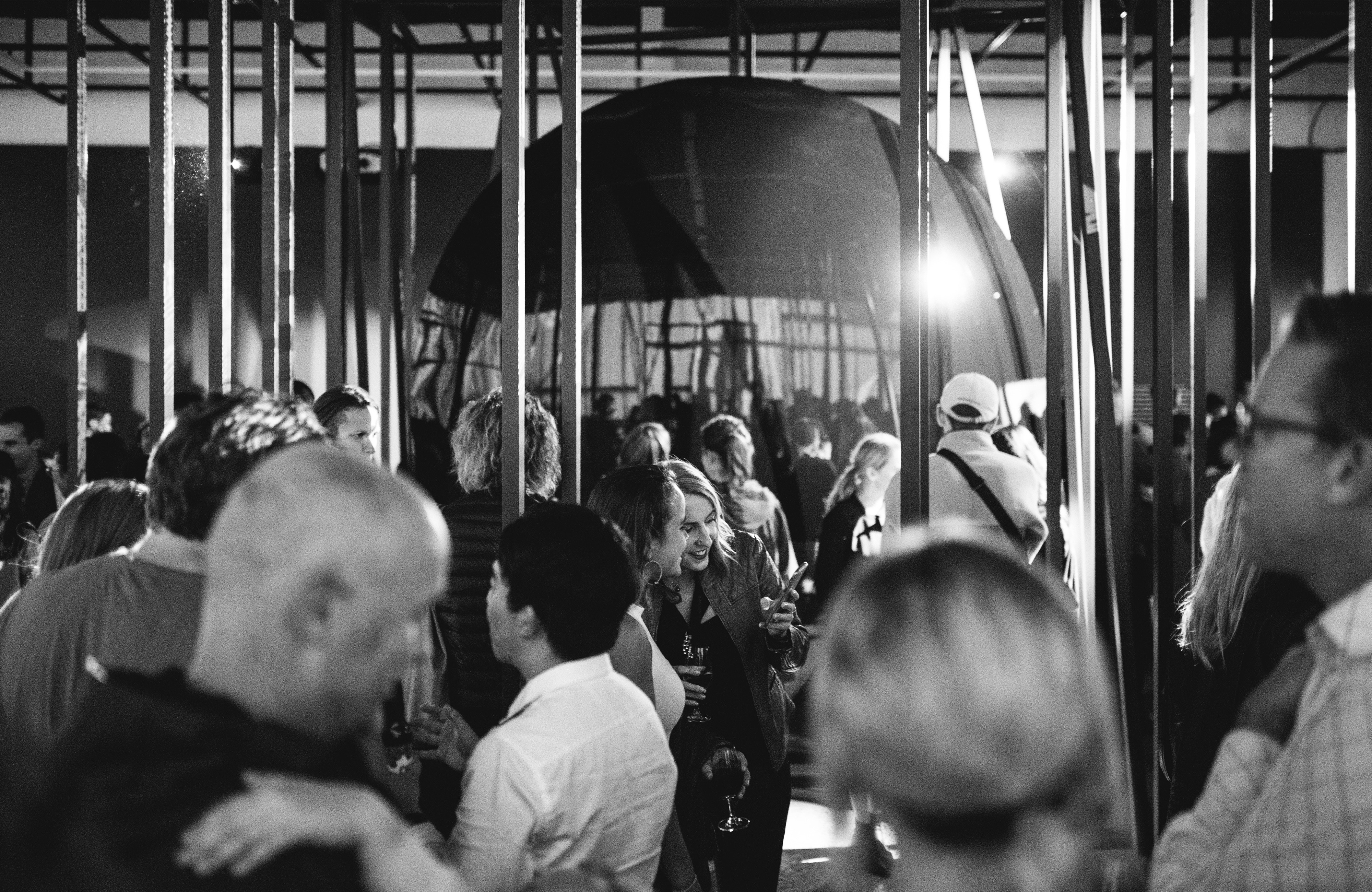 A man crowd stand around talking in front of a huge curved piece of glass.