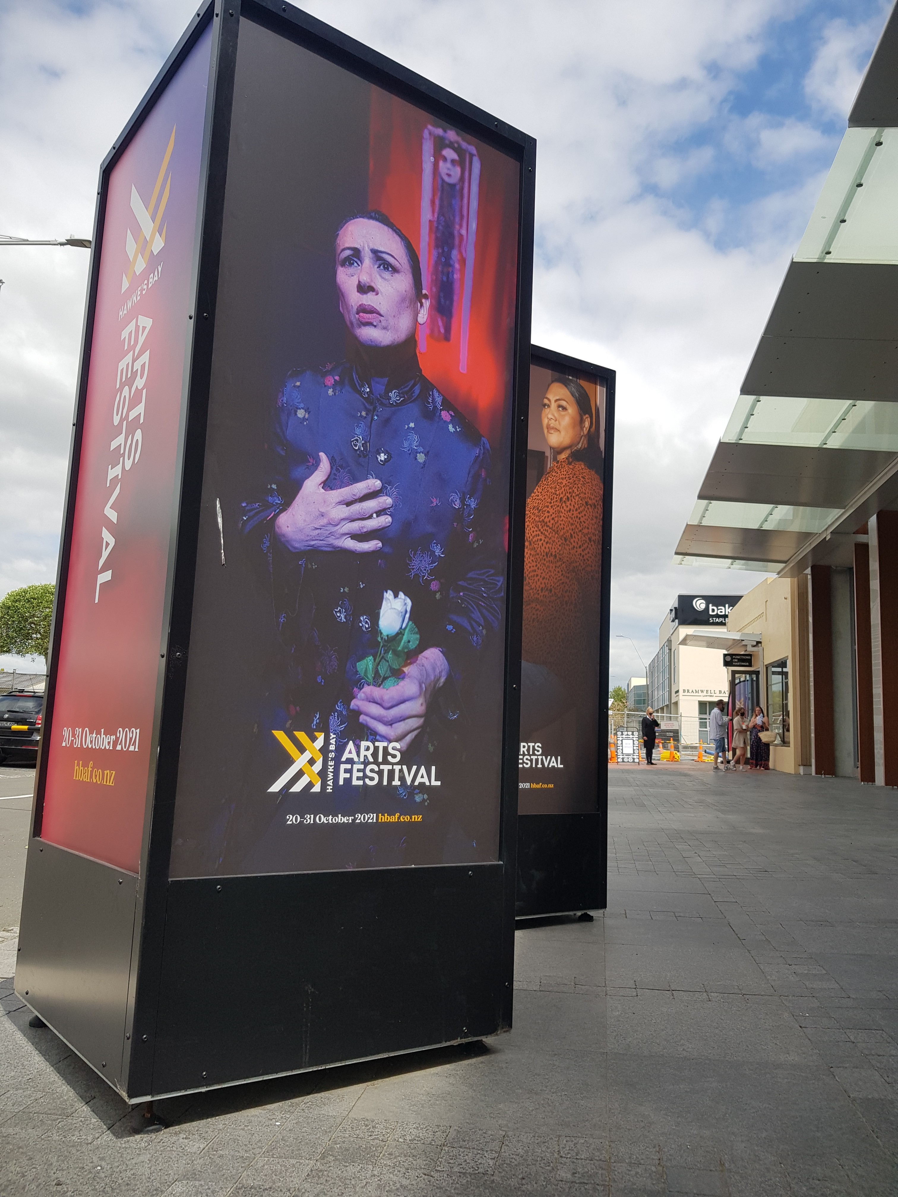 On a street, a four-sided plinth displays advertising with an image of a Chinese woman in costume.