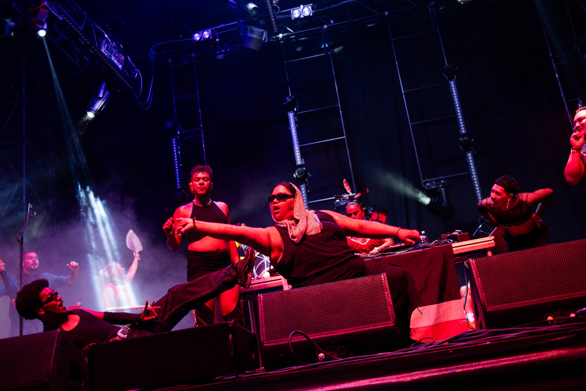 An action shot of performers having a good time while voguing on stage in front of a DJ who is busy playing music