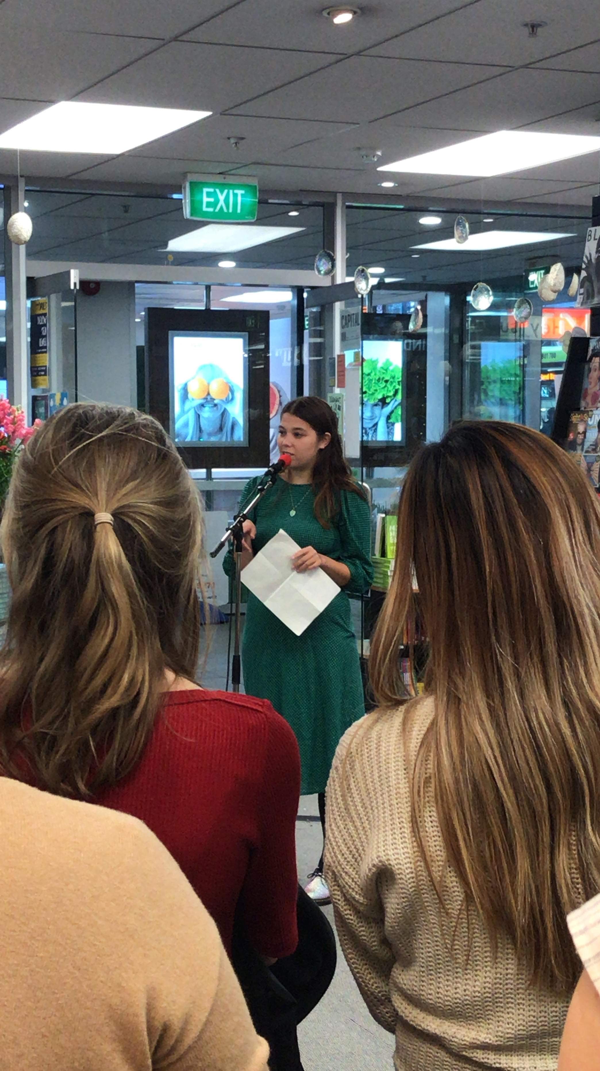 Nina Mingya Powels speaks at a microphone in a crowded book shop.