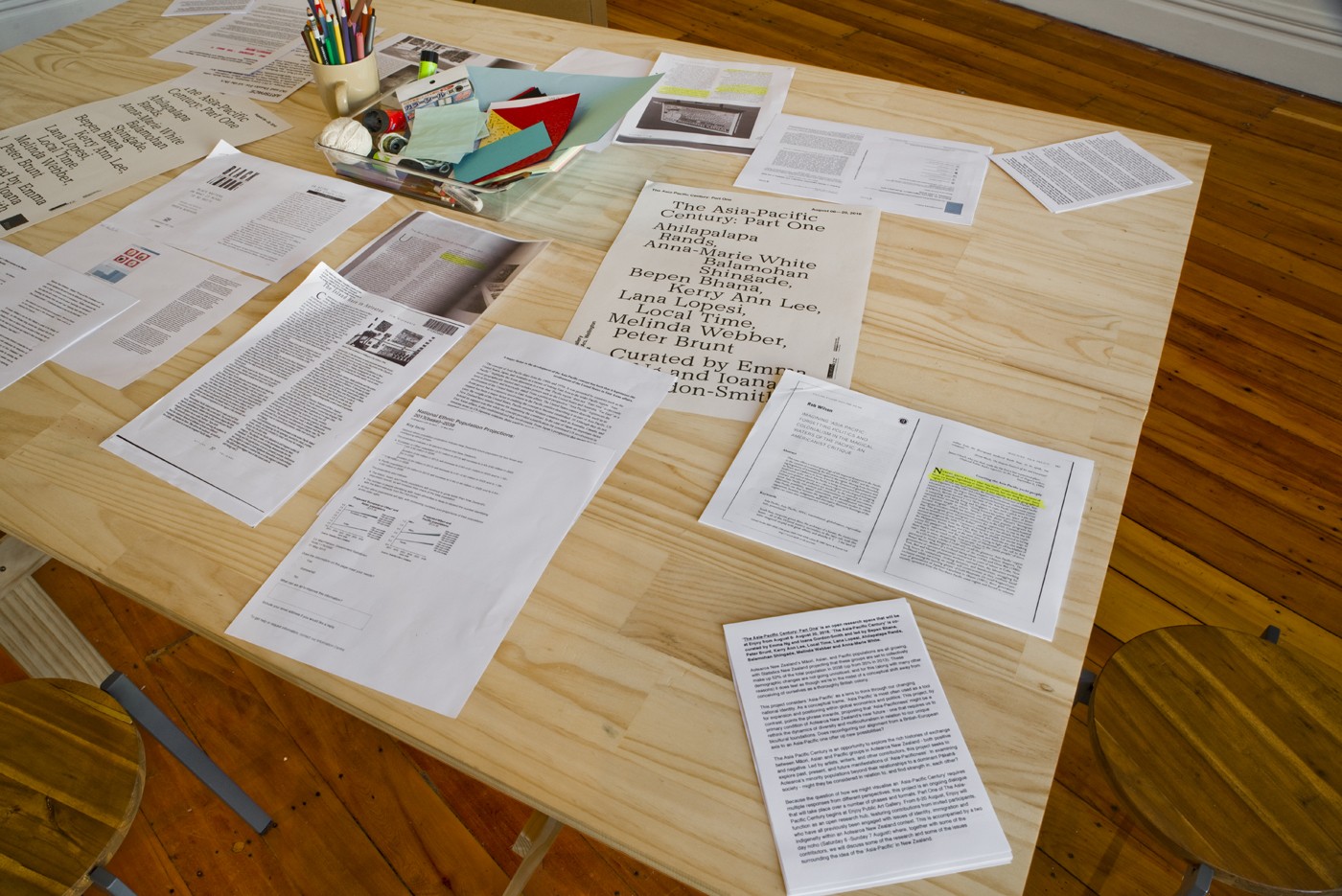 Photocopied articles and other research papers are scattered across a table in an art gallery.