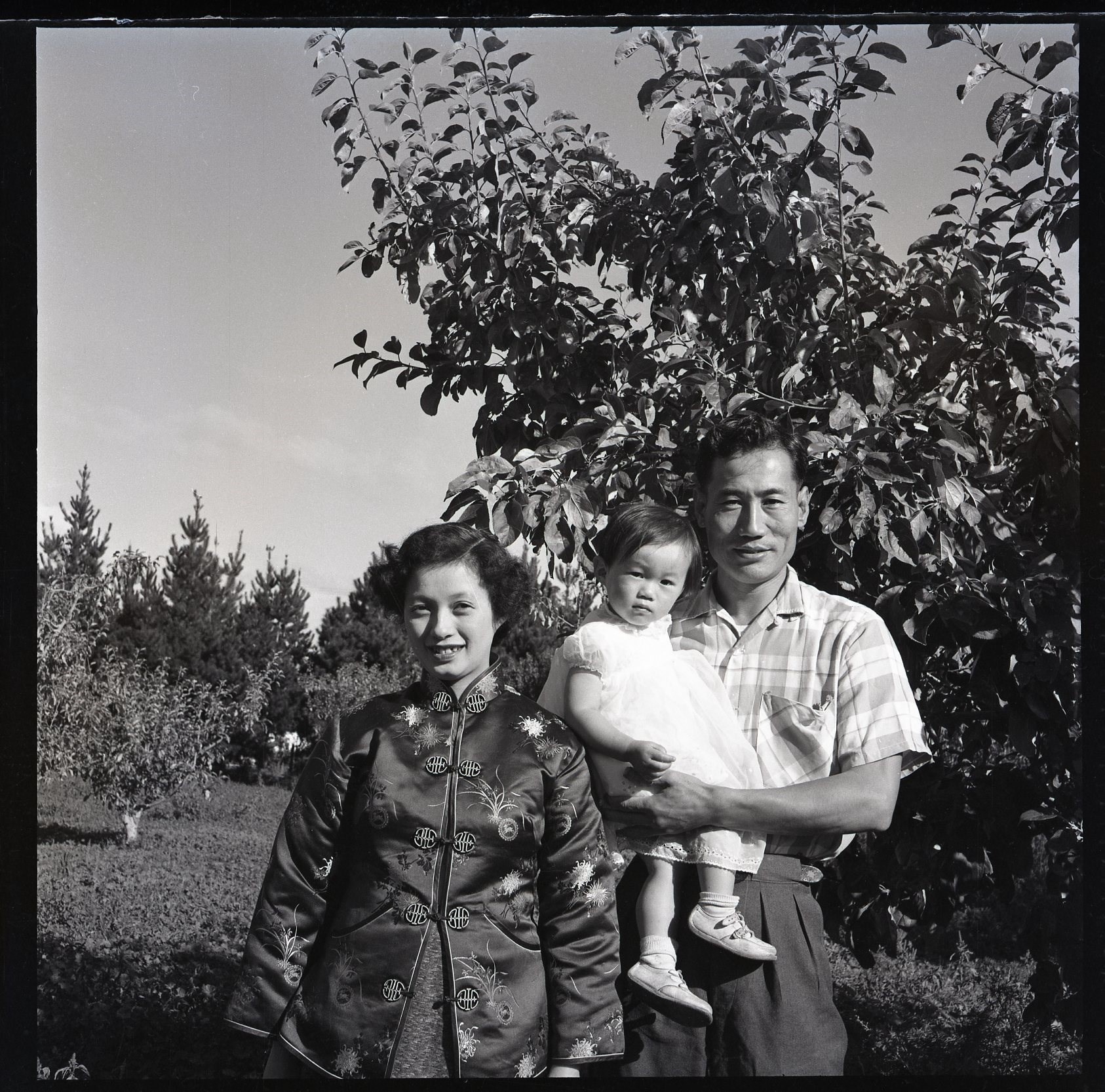 Black and white family photograph with infant daughter, in an orchard.