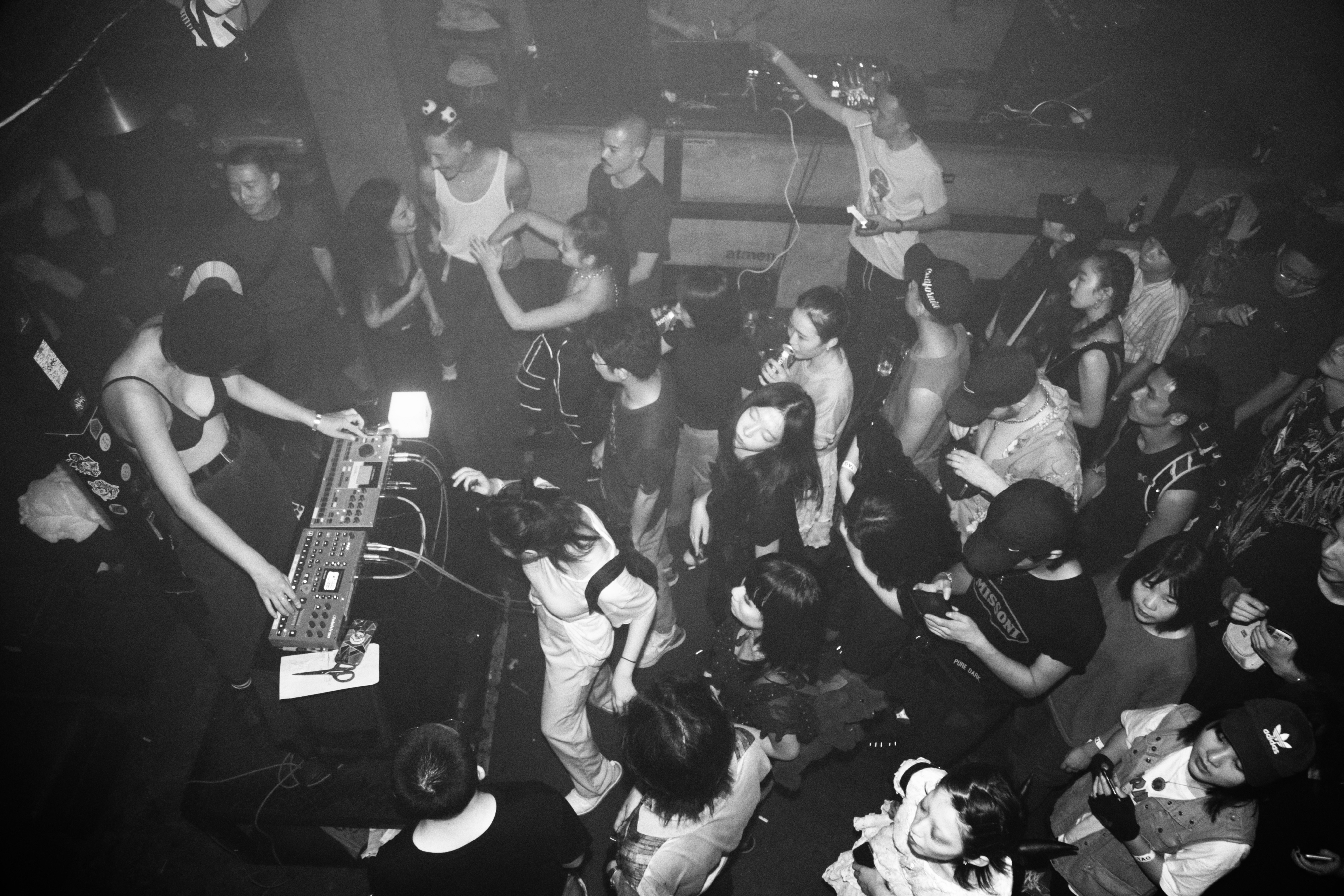 An overhead view of people dancing around a DJ stage, taken in black and white