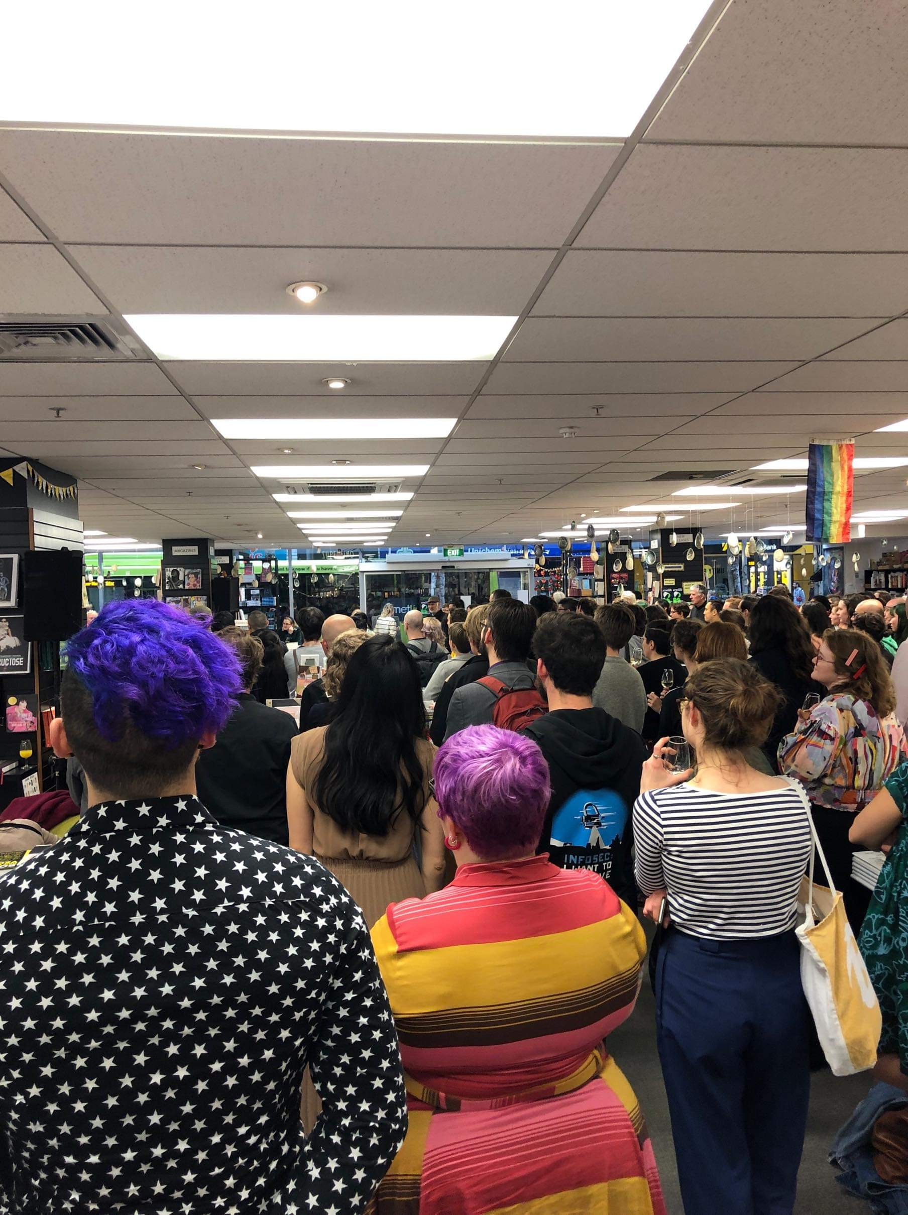 A crowd of people stand listening to speeches in a book shop.