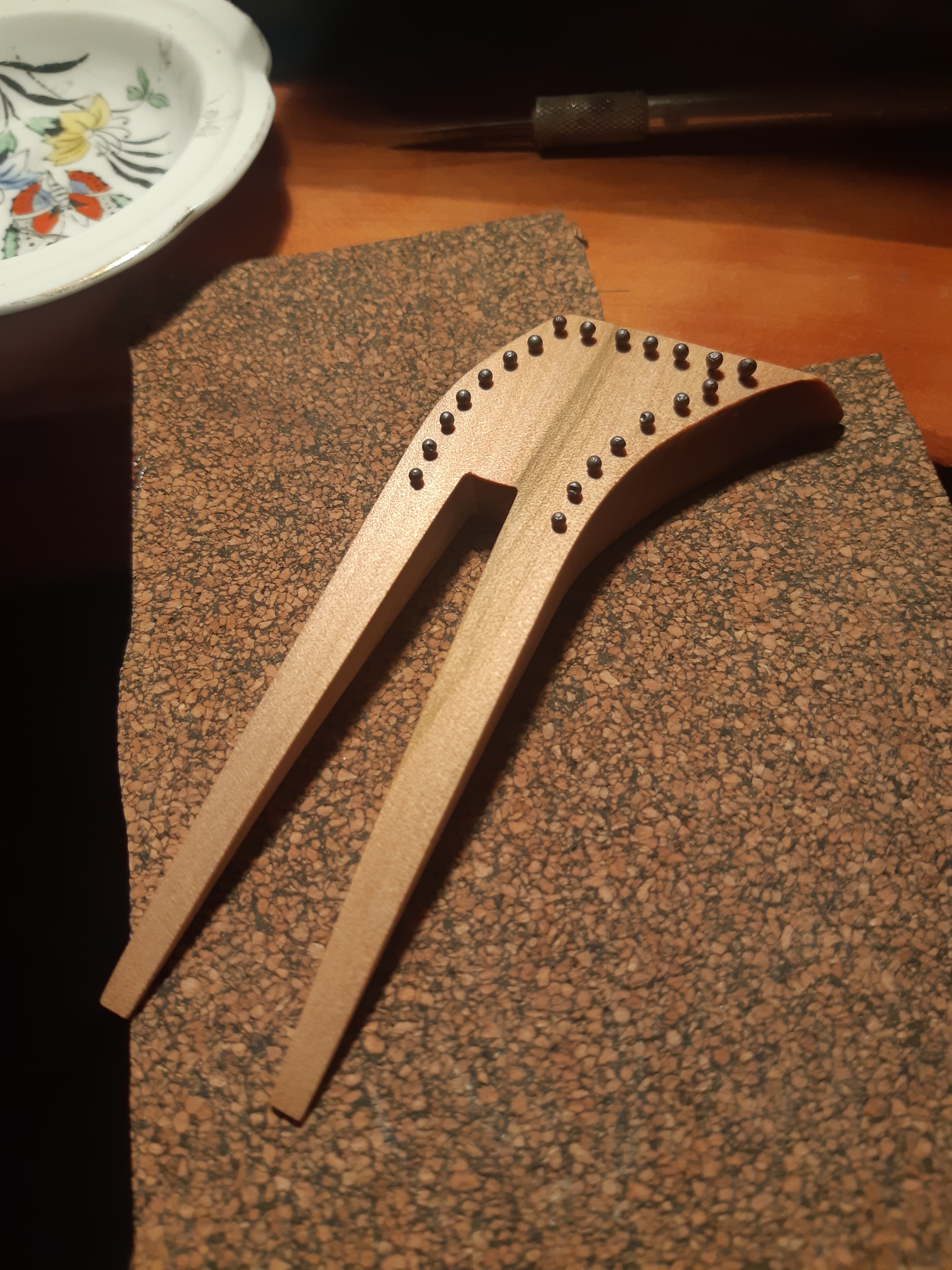 An unfinished kanzashi on top of a brown mat, with a tool in the corner