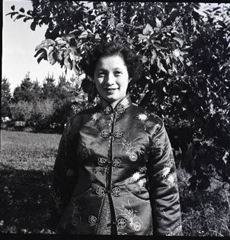 A Chinese woman in a Chinese silk jacket stands in an orchard.