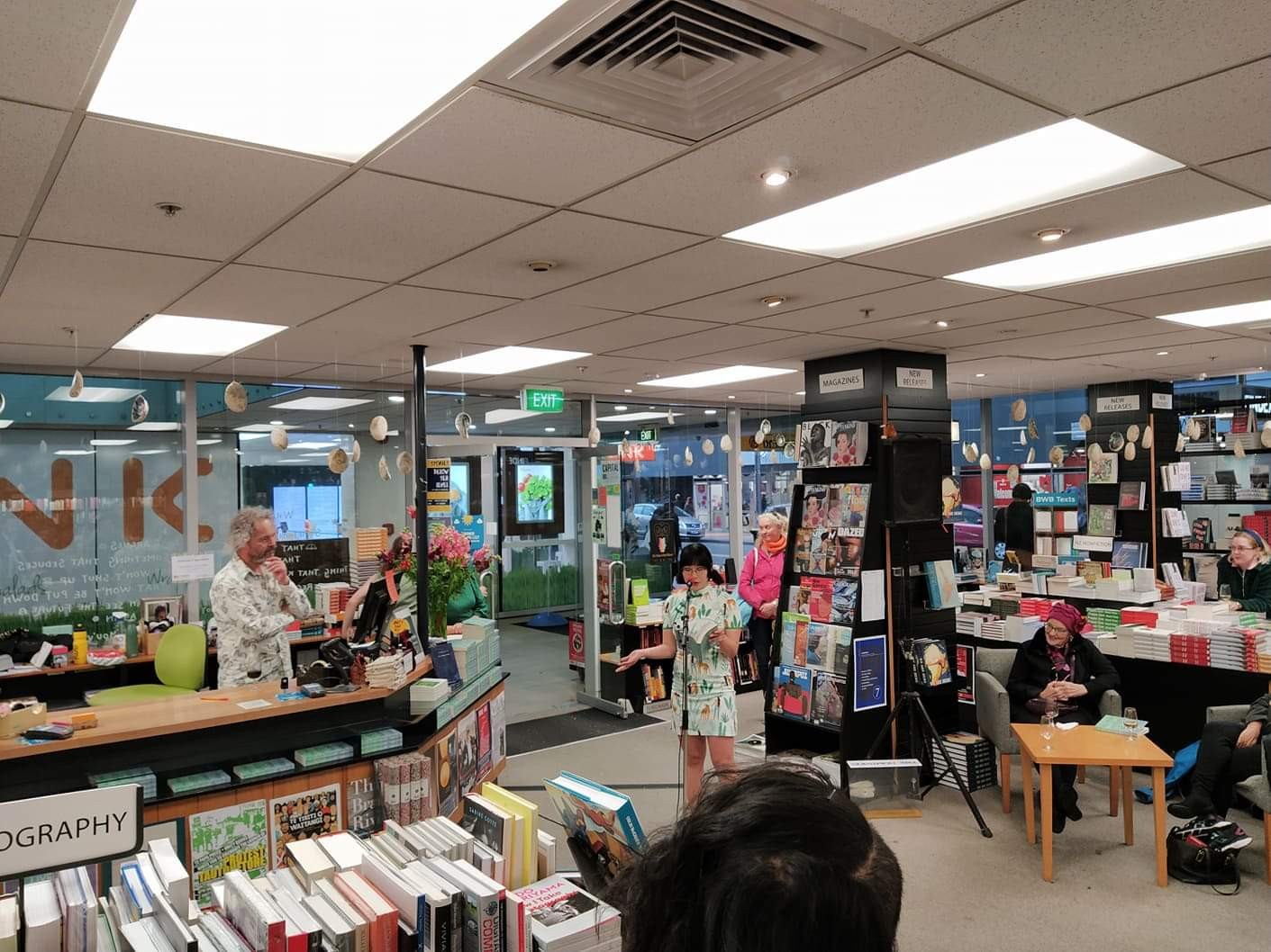 Rose Lu reading from her book at a microphone in a book shop.