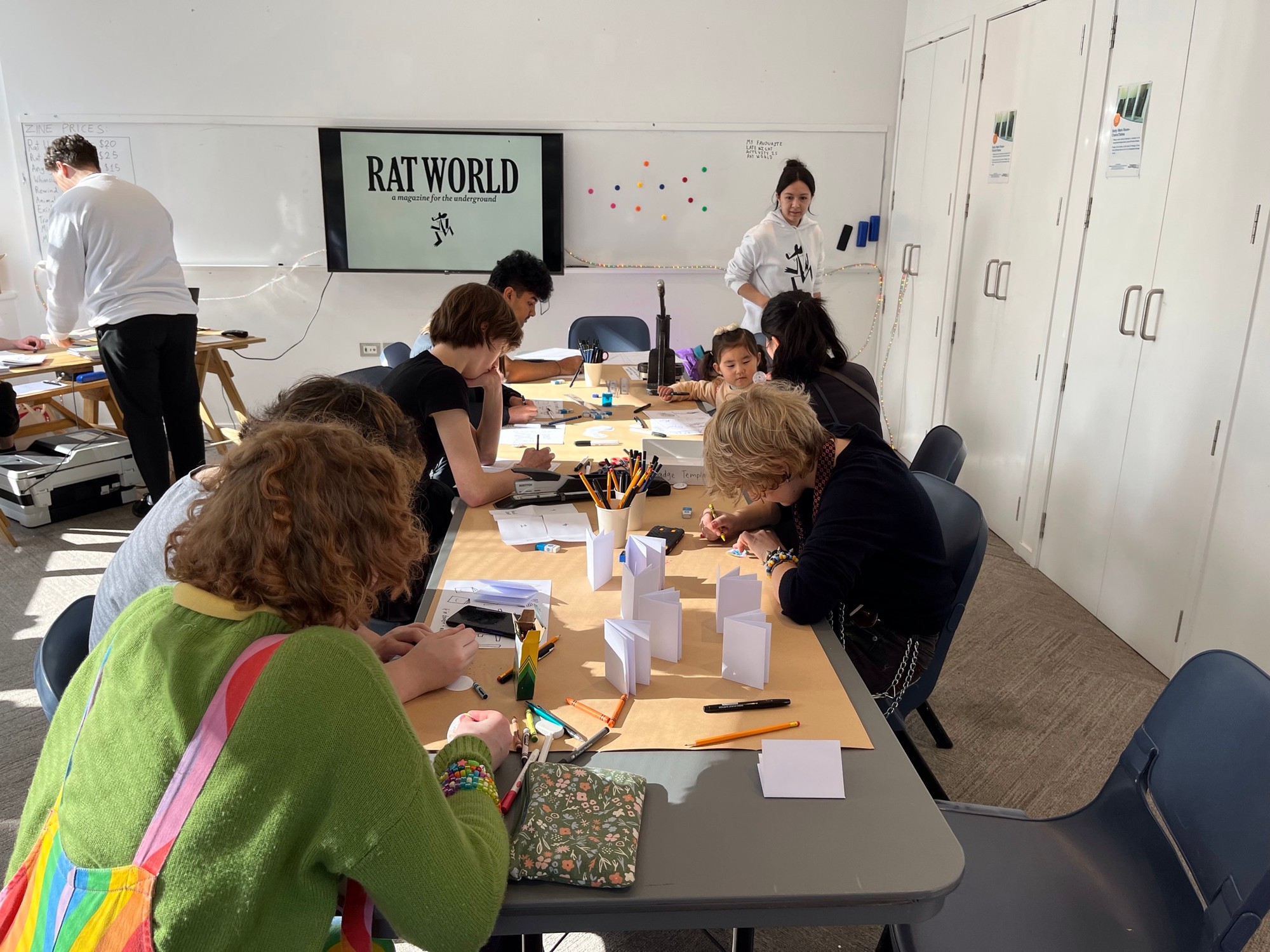 People gathered around a table with paper and pens to make zines.