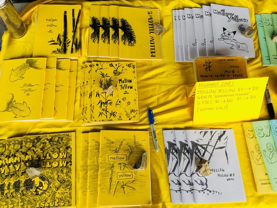Various colourful zines laid on top of a yellow tablecloth.