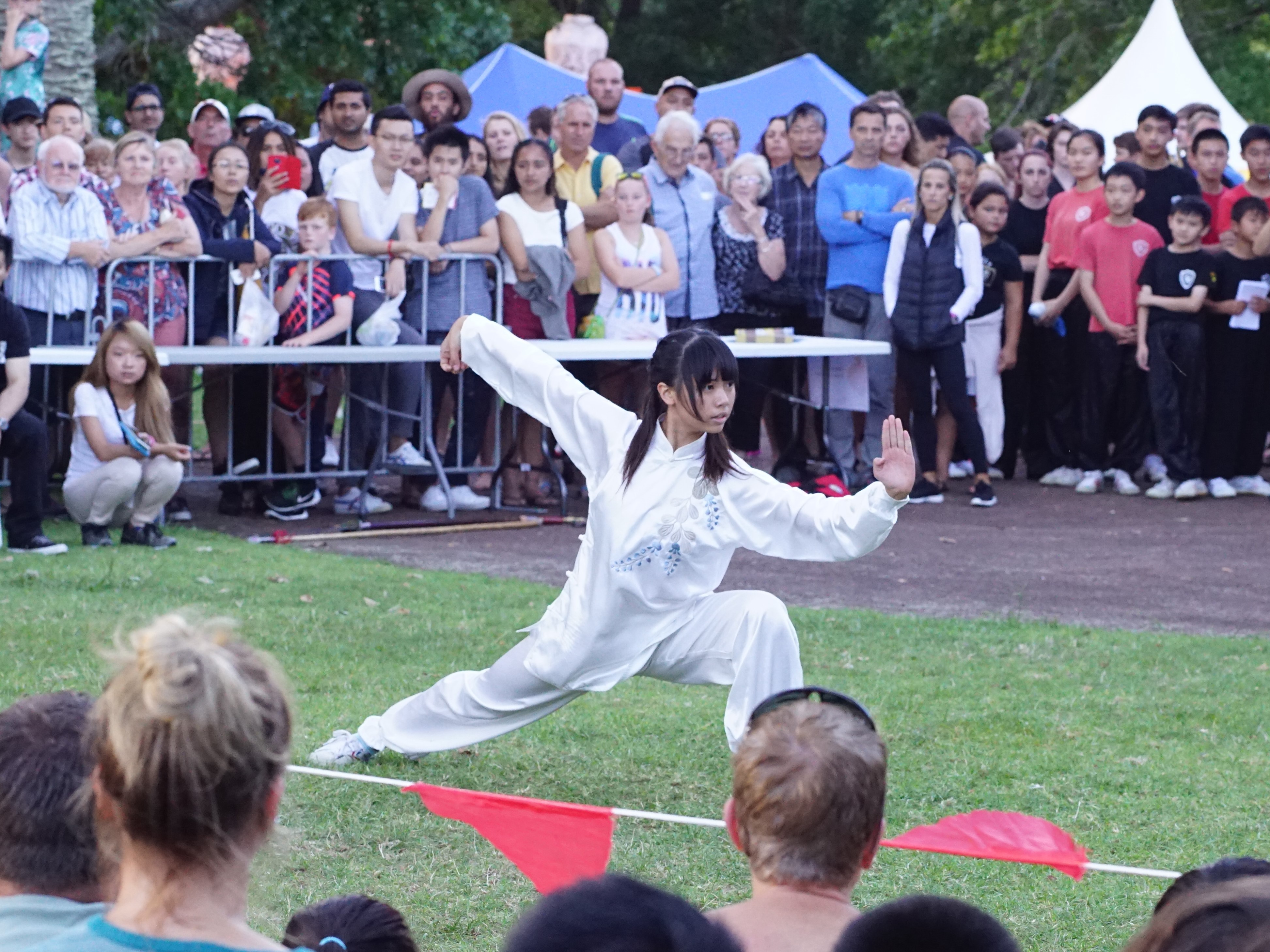 a distant shot of an asian women wearing white Wushu costume performing in a competition