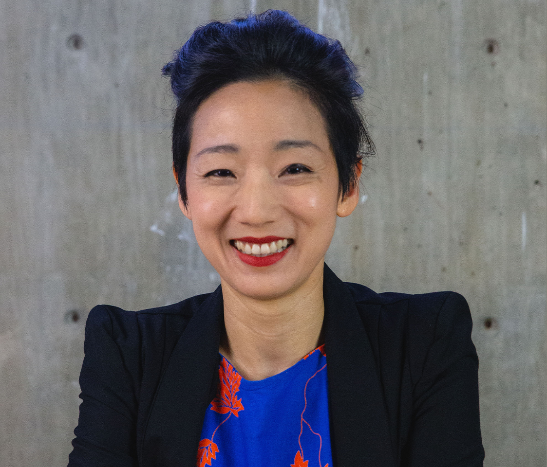 Smiling Liyen Chong wearing red lipstick and a blazer with a colourful printed top.