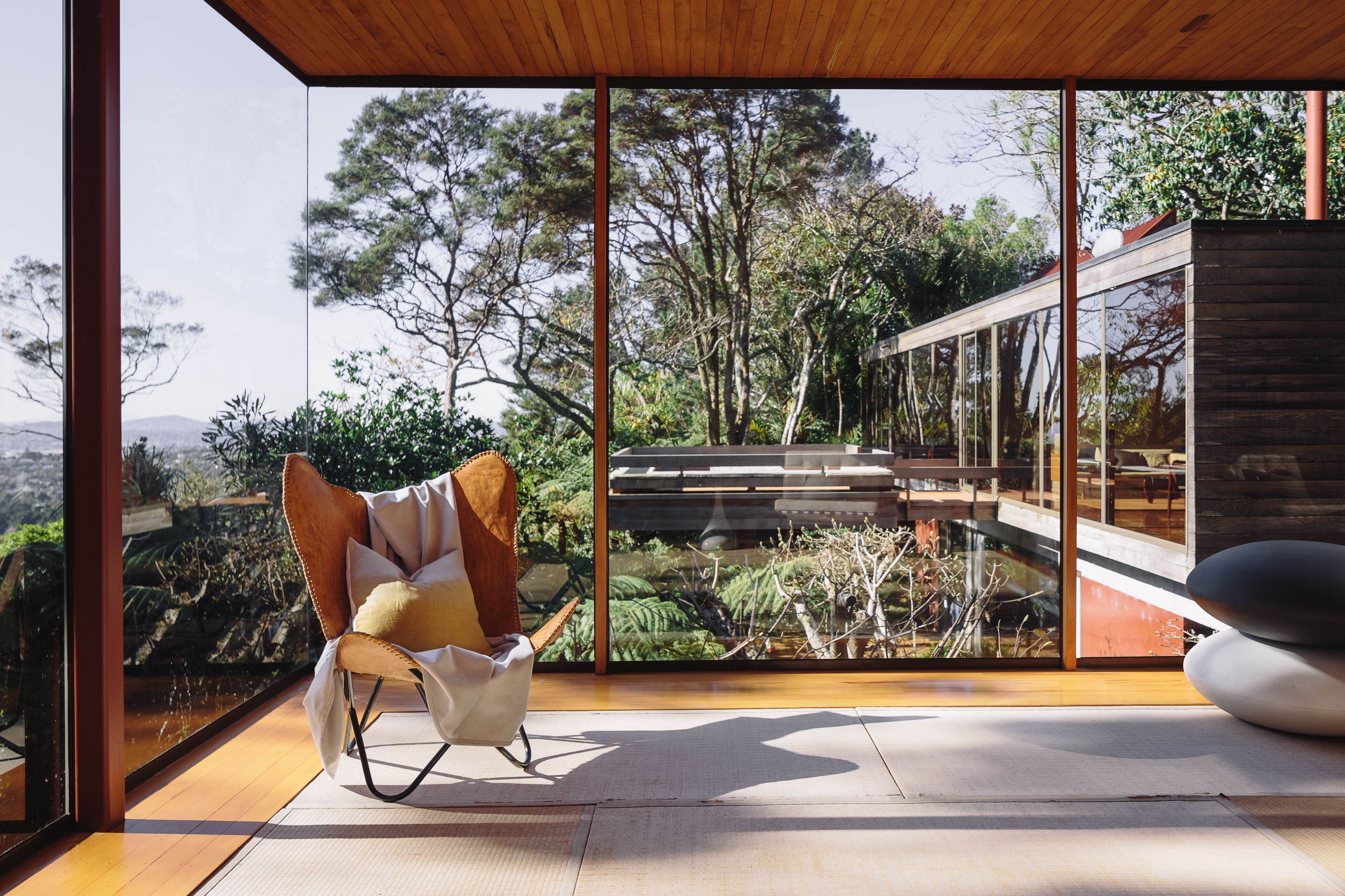 A chair in a room with floor-to-ceiling windows with trees in the background