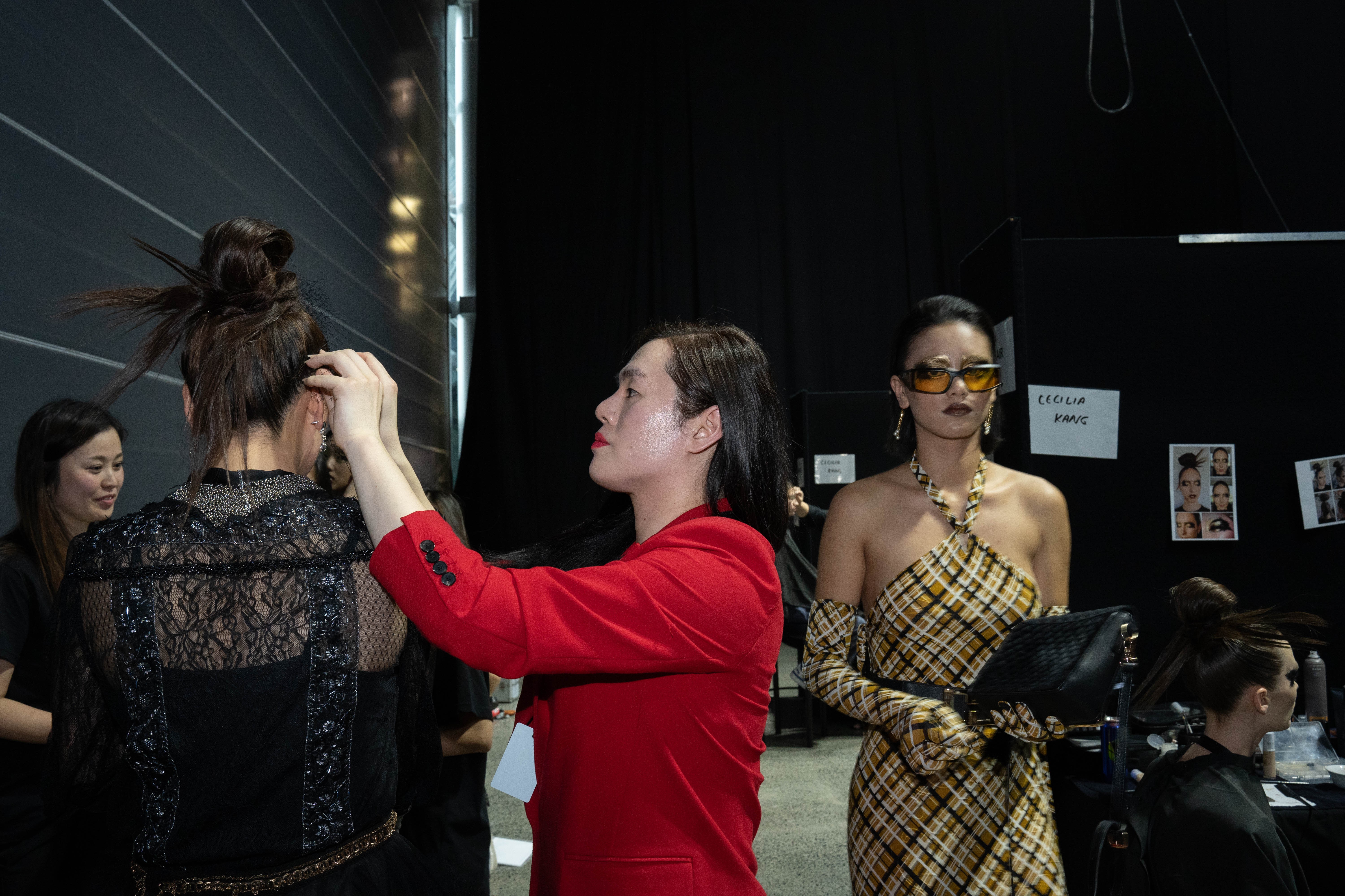 A woman in red fixing the hair of a model in a black dress