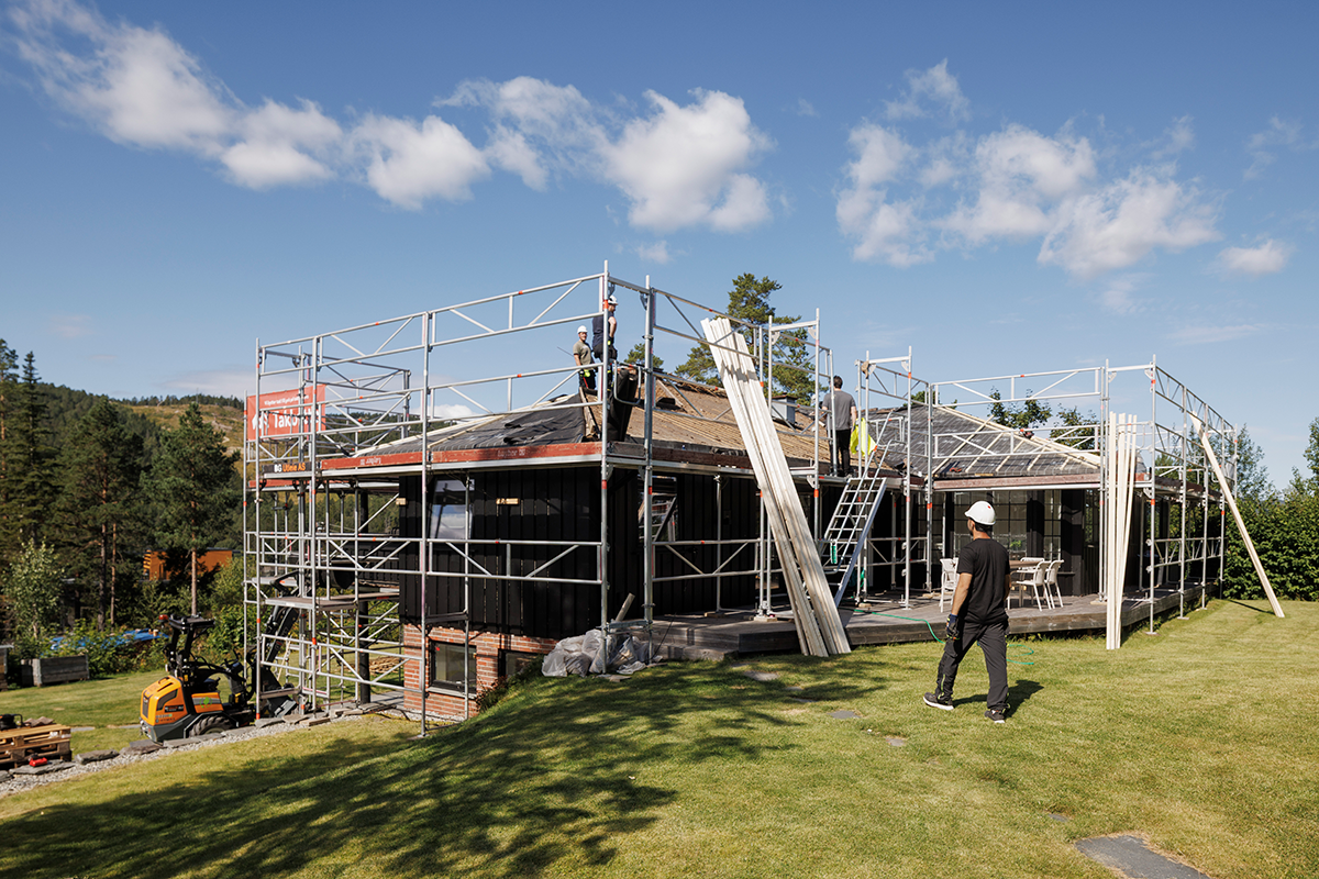 Tømrere som bytter tak på en enebolig med stillas rundt bygget