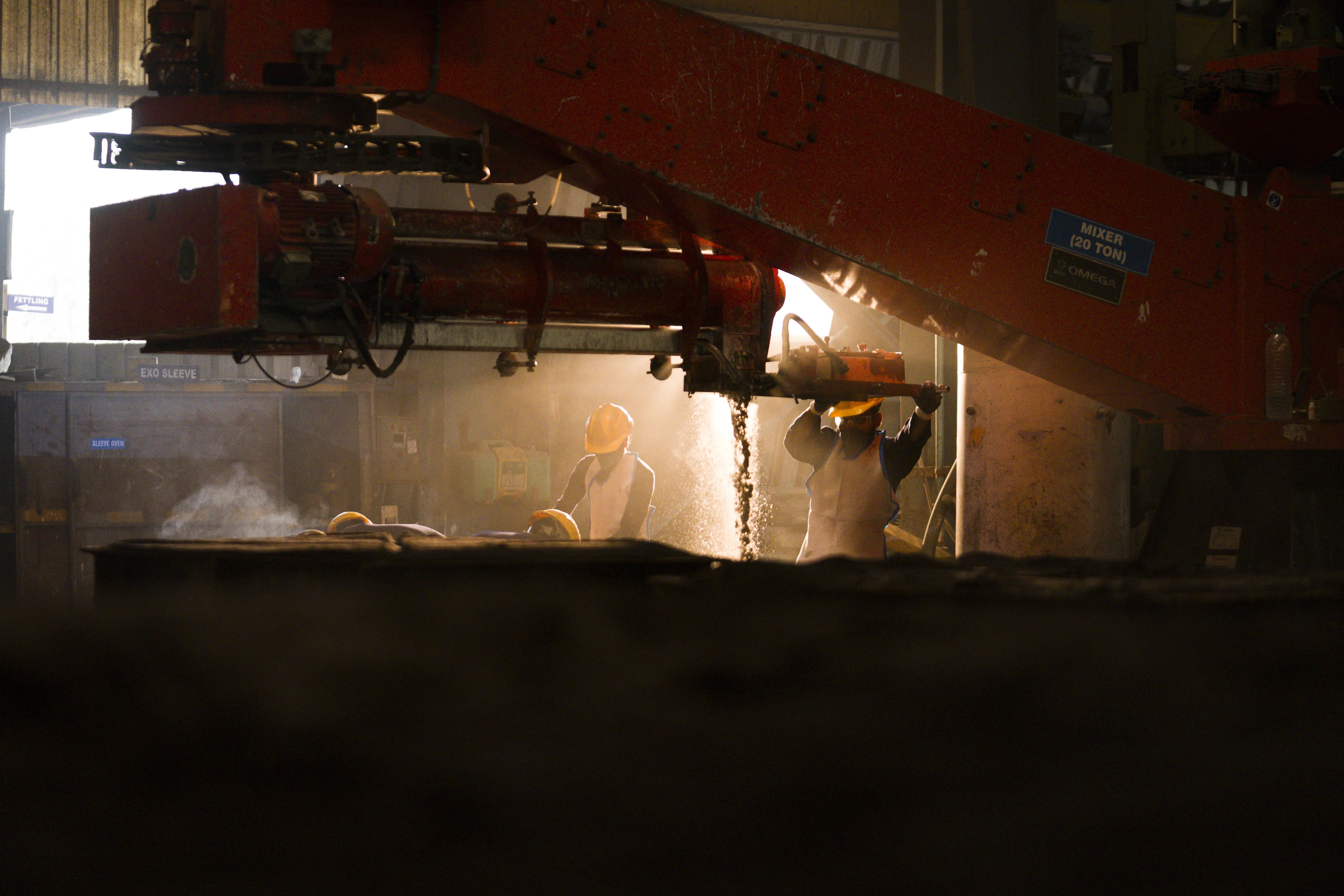 Workers operating sand mixer for mould preparation in foundry