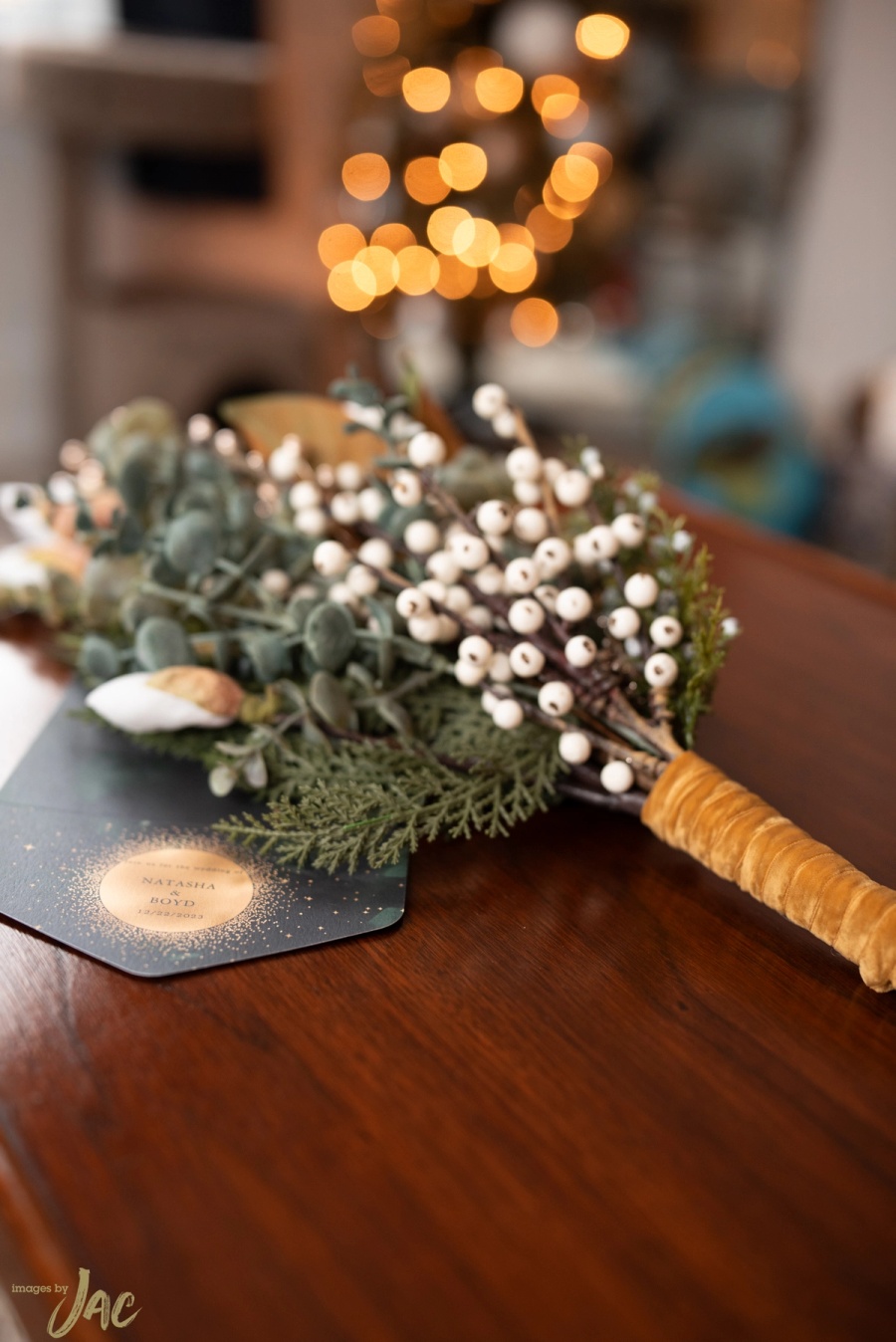 A winter bouquet of white berries, eucalyptus and cedar with a gold-wrapped handle, on a wooden table